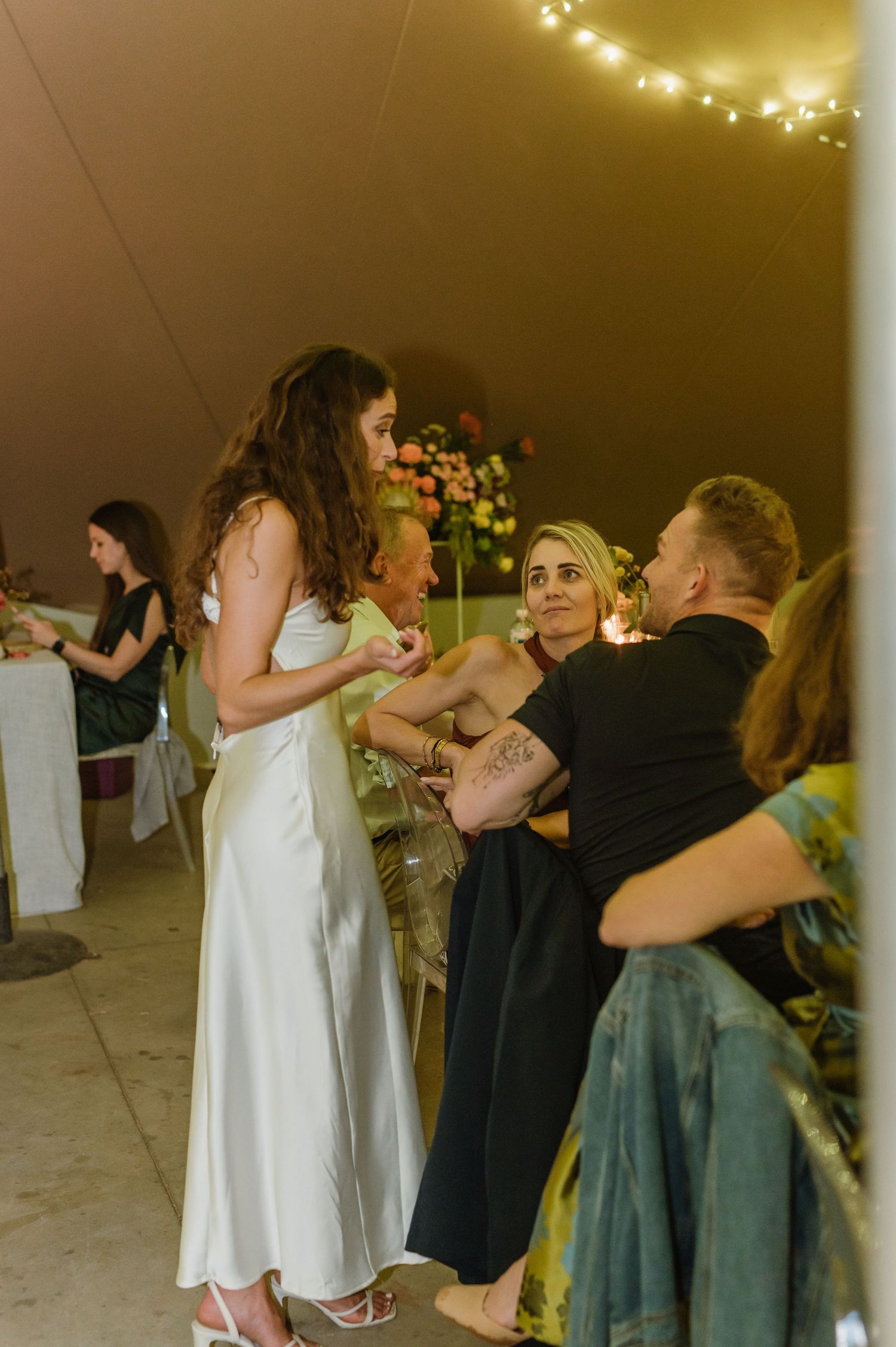 Wedding guests dancing and celebrating together under warm string lights at an indoor reception venue.