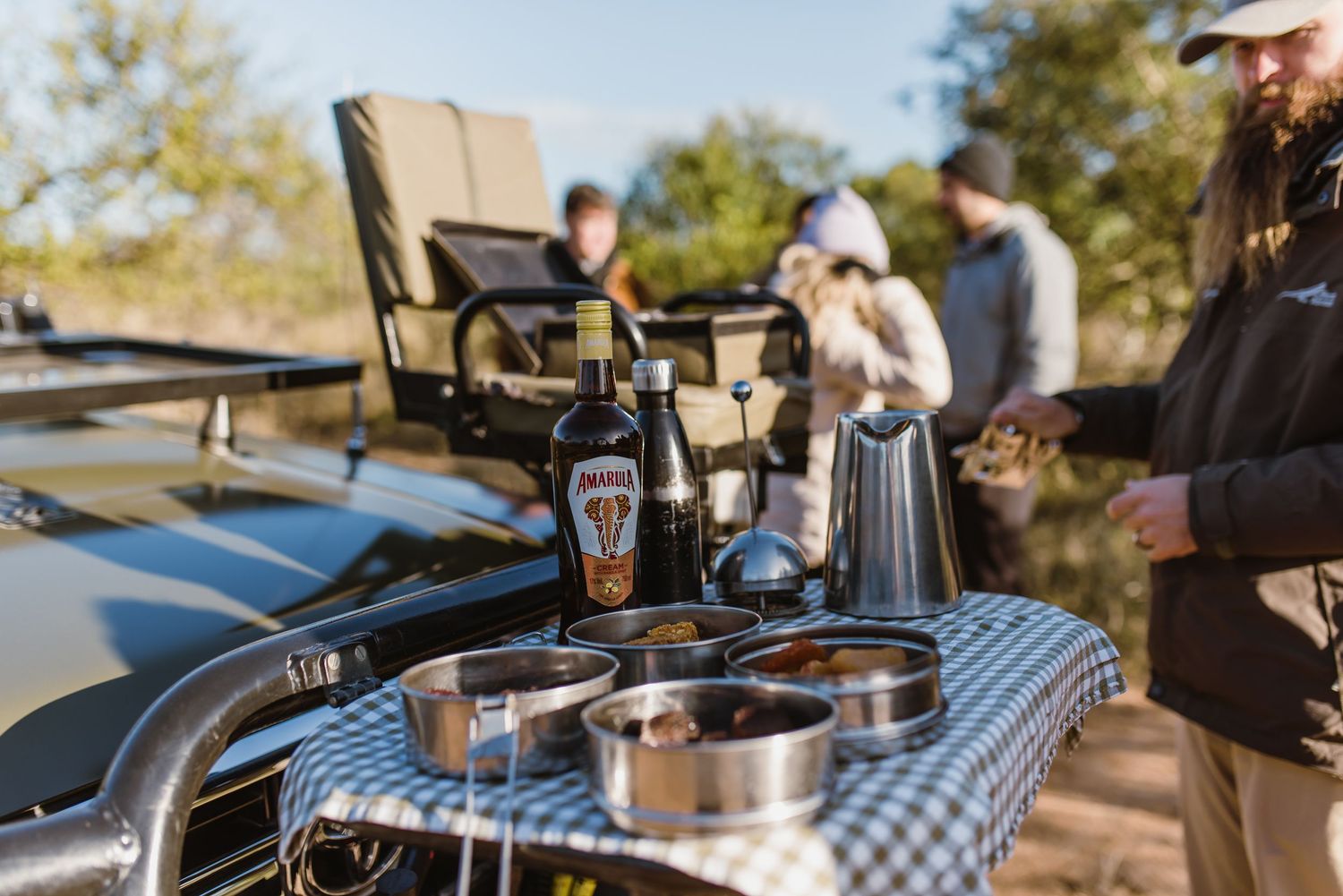 Outdoor coffee brewing setup with kettles and equipment arranged on wooden tables during a sunny day in nature.