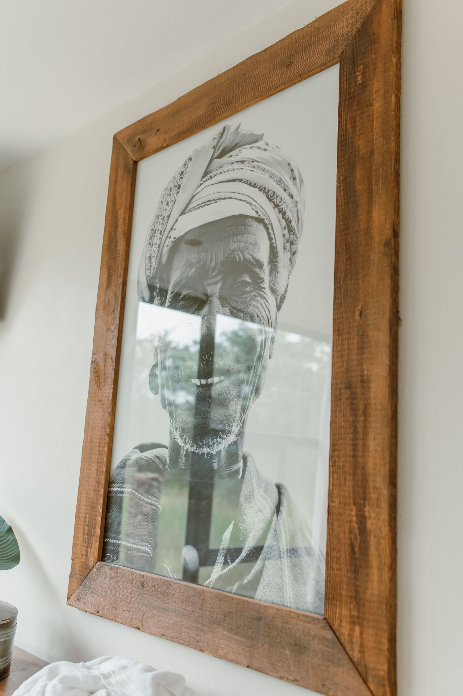 Black and white portrait photograph in rustic wooden frame showing figure wearing traditional headwrap.