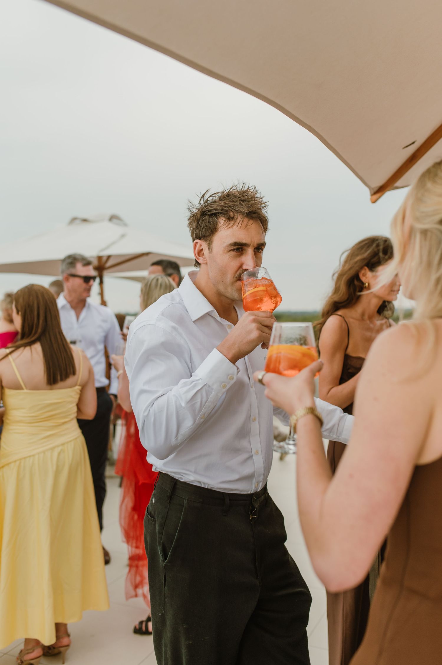 Wedding reception guests mingling and dancing under a white tent with yellow and coral colored dresses.