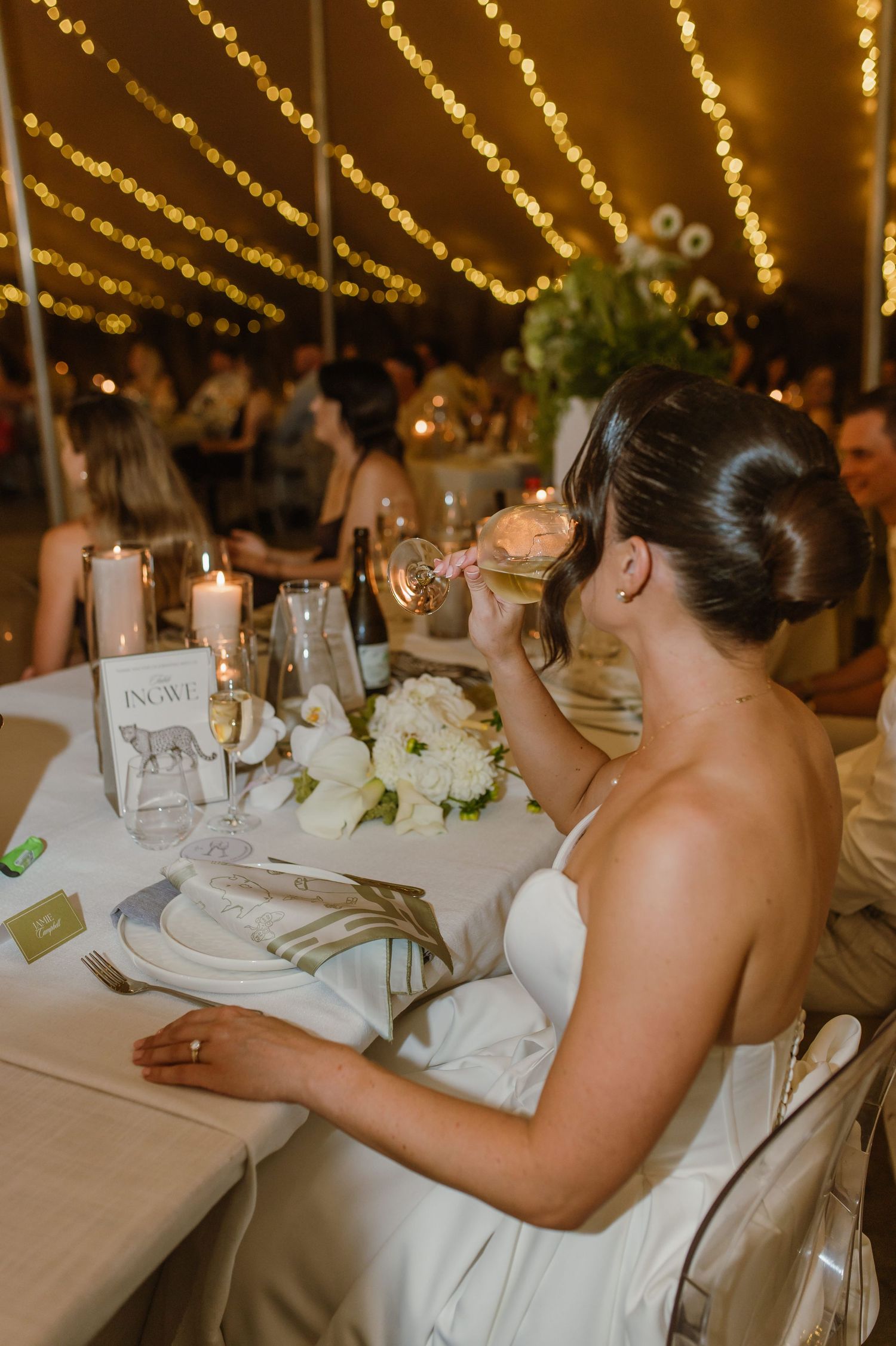 Elegant wedding reception dinner with string lights glowing overhead and white floral centerpieces.