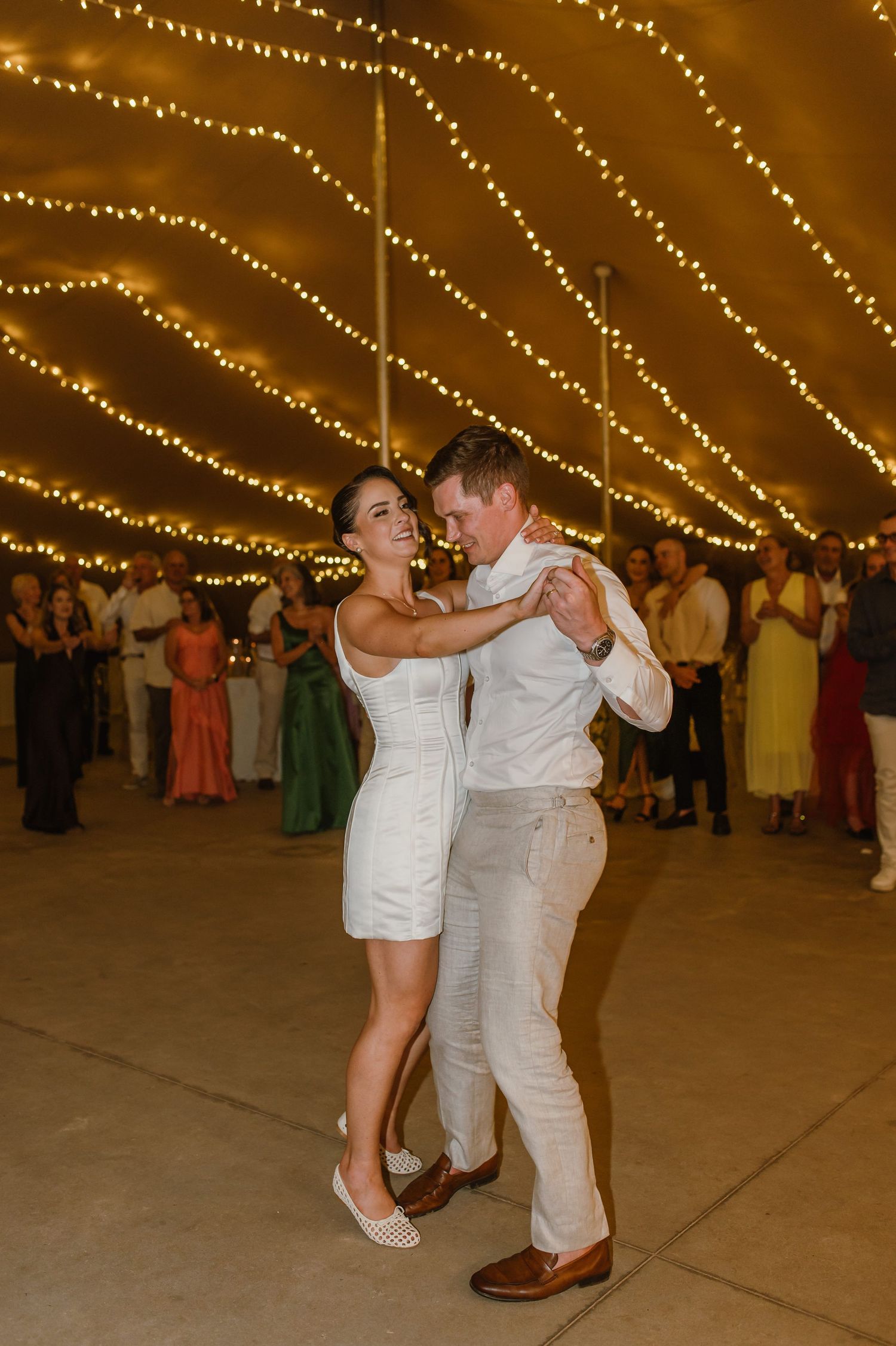 Couple dancing together under string lights at an elegant wedding reception.