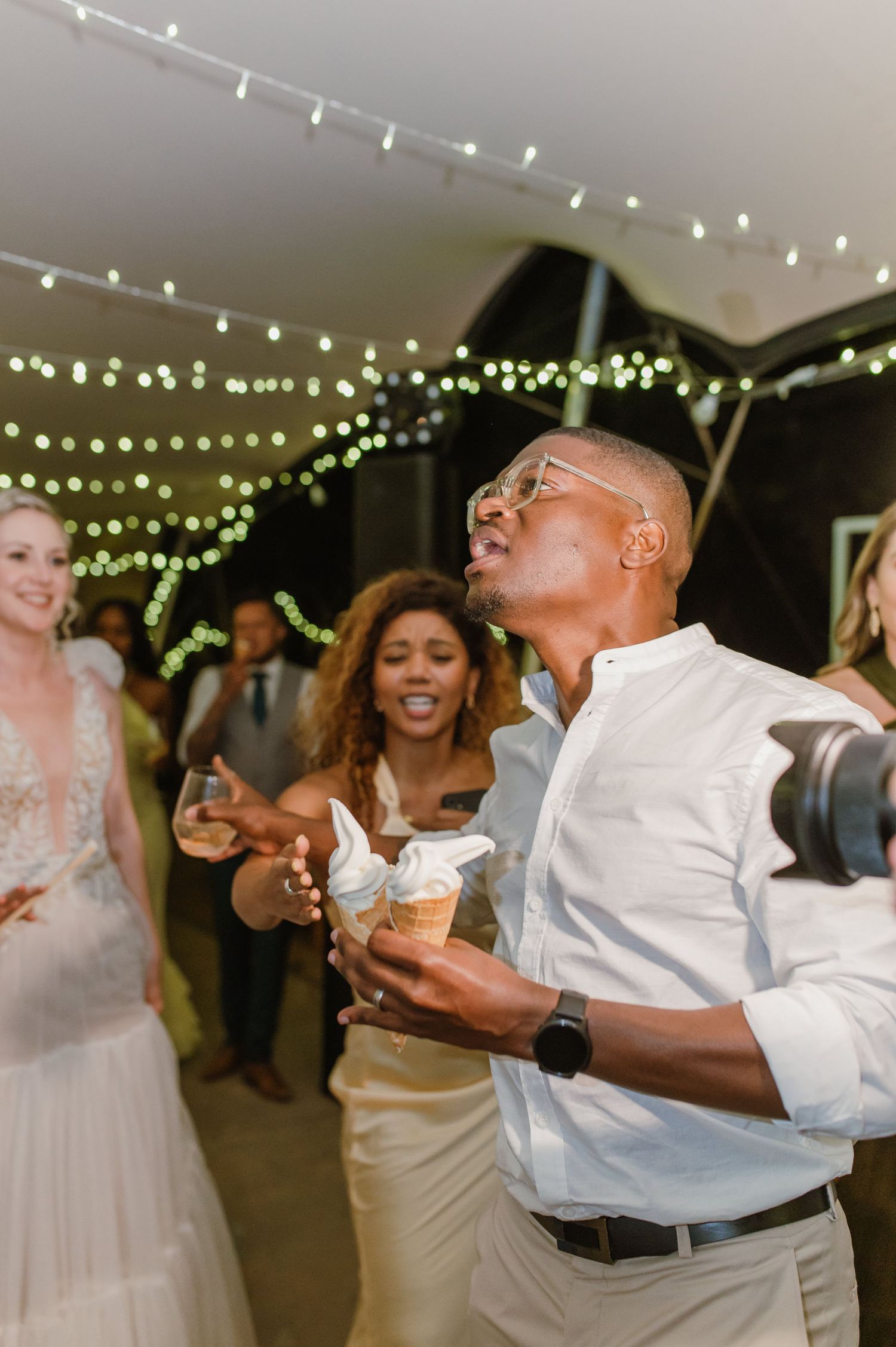 Wedding guests dancing under twinkling string lights at an evening reception celebration.