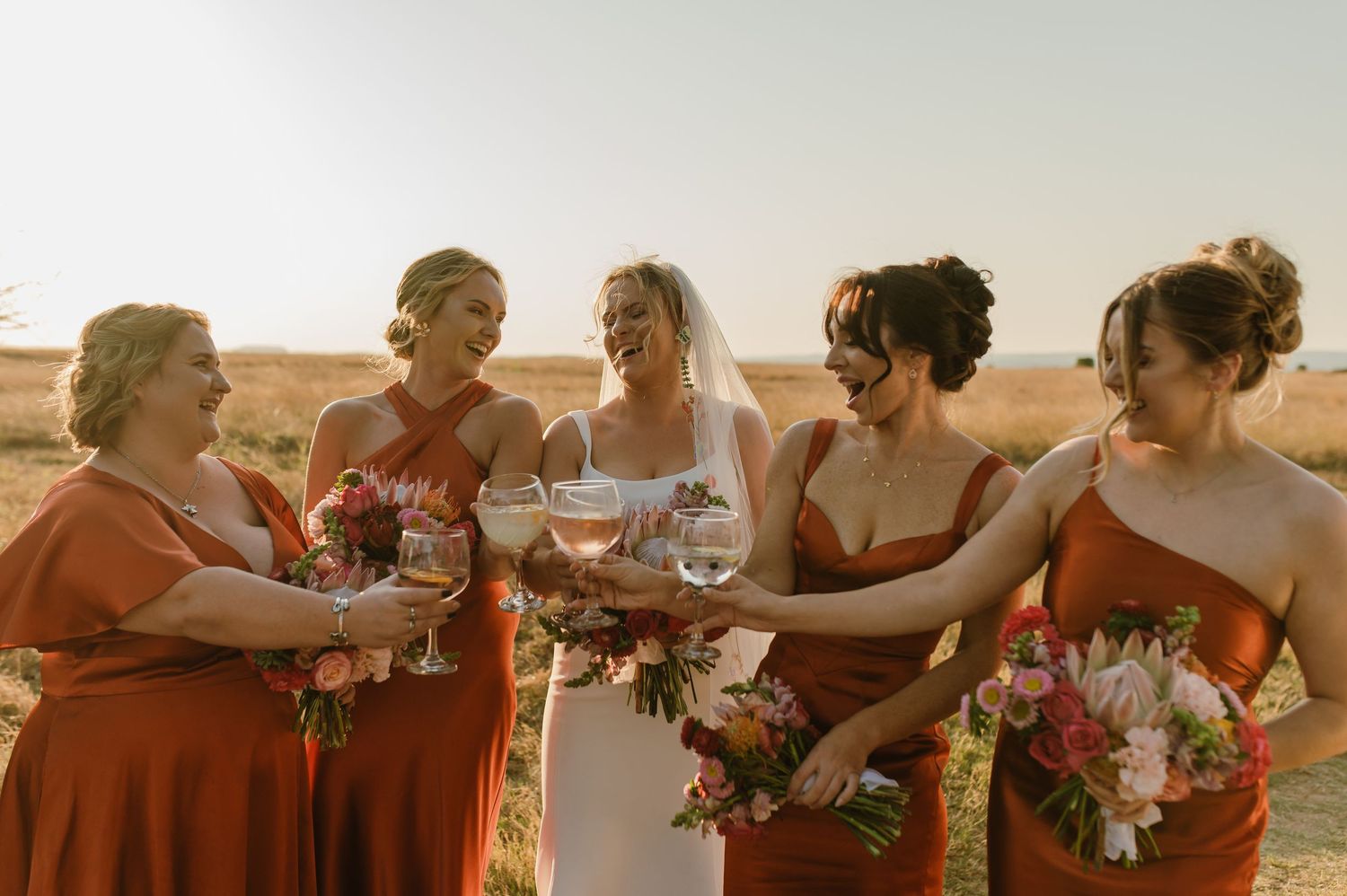 Wedding party shares candid moments and laughter during sunset photo session.