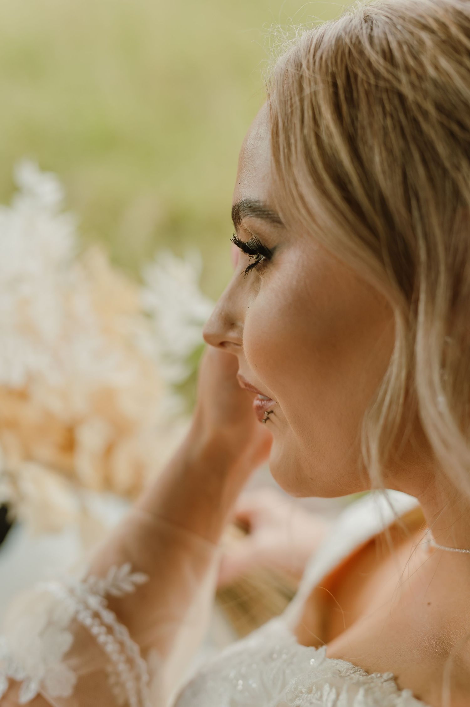 Close-up profile view of a bride with blonde hair wearing a lace wedding dress and natural makeup.