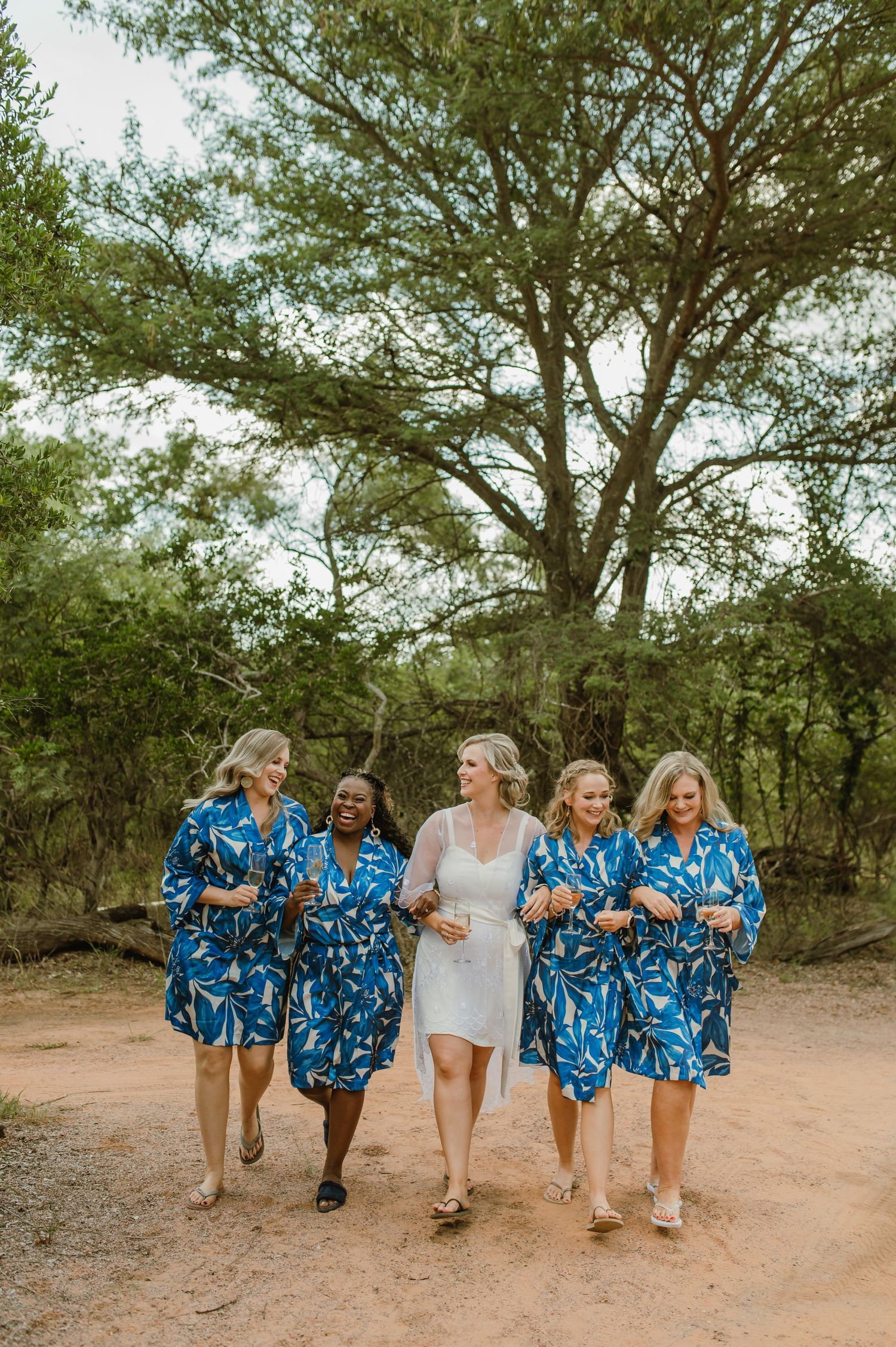 Bridal party wearing matching blue floral robes walking together on outdoor path.