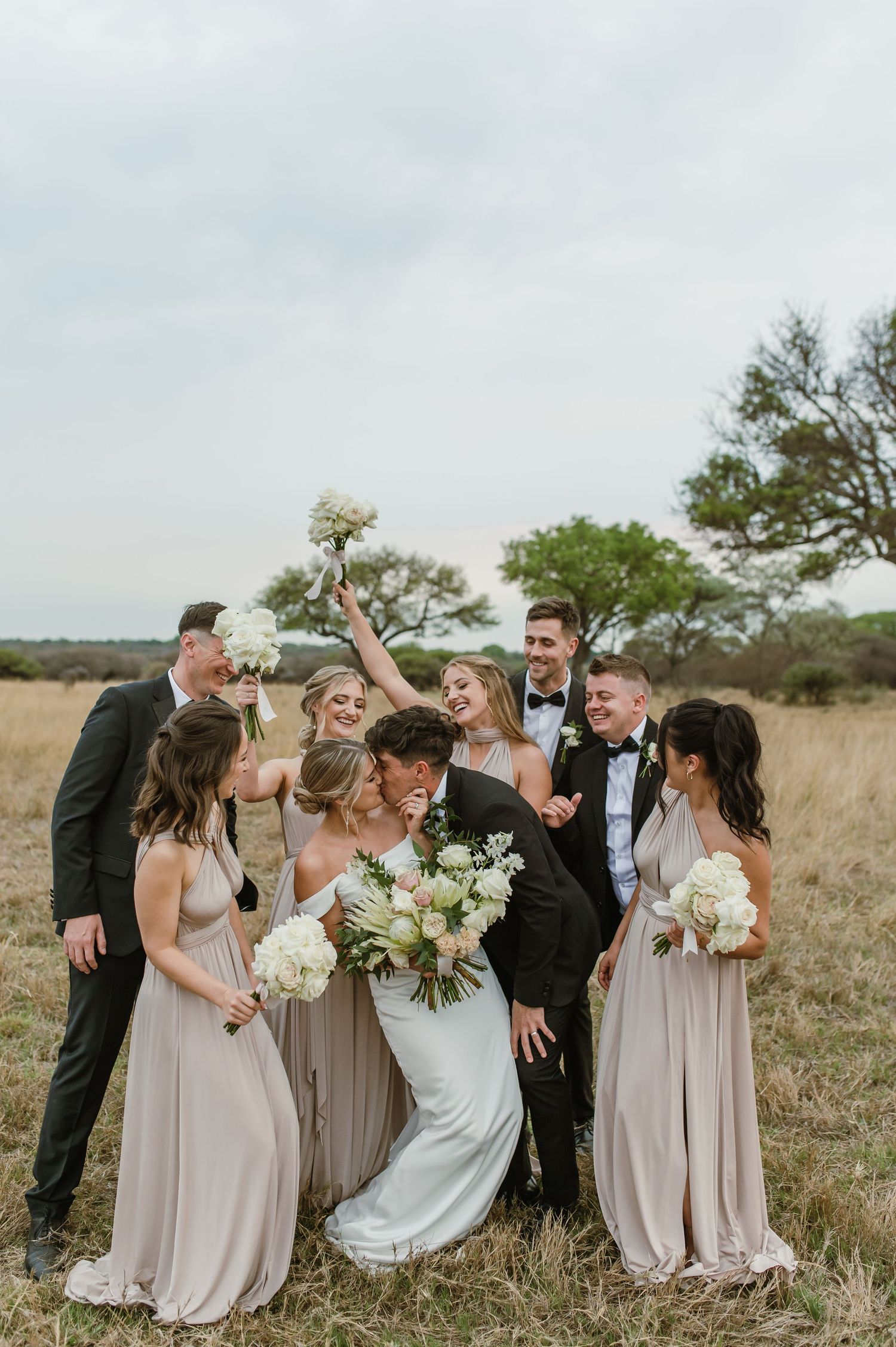Wedding party shares candid laughs and celebrations in an outdoor field setting.