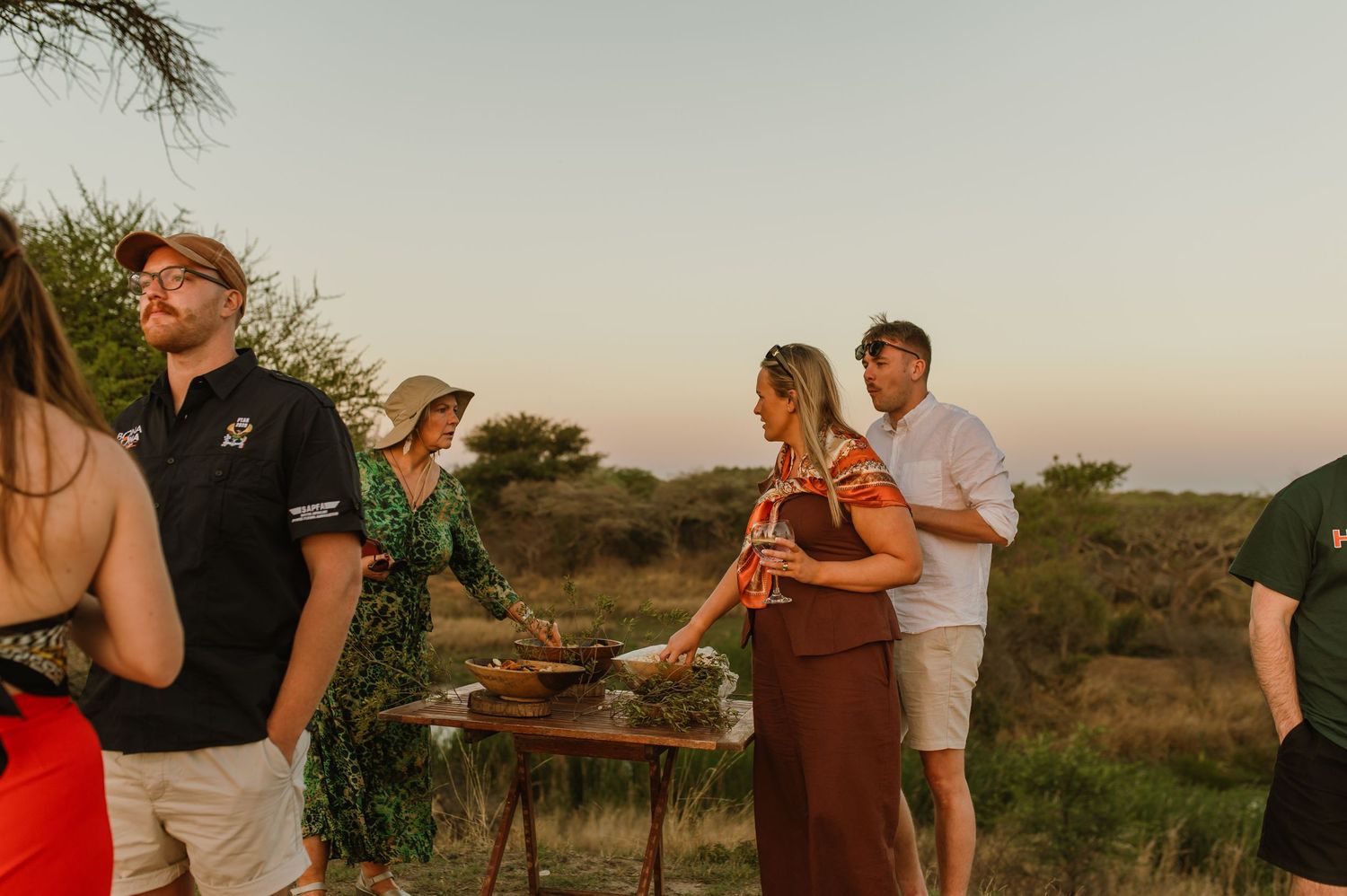 Outdoor safari sundowner event with guests enjoying drinks and snacks at dusk.