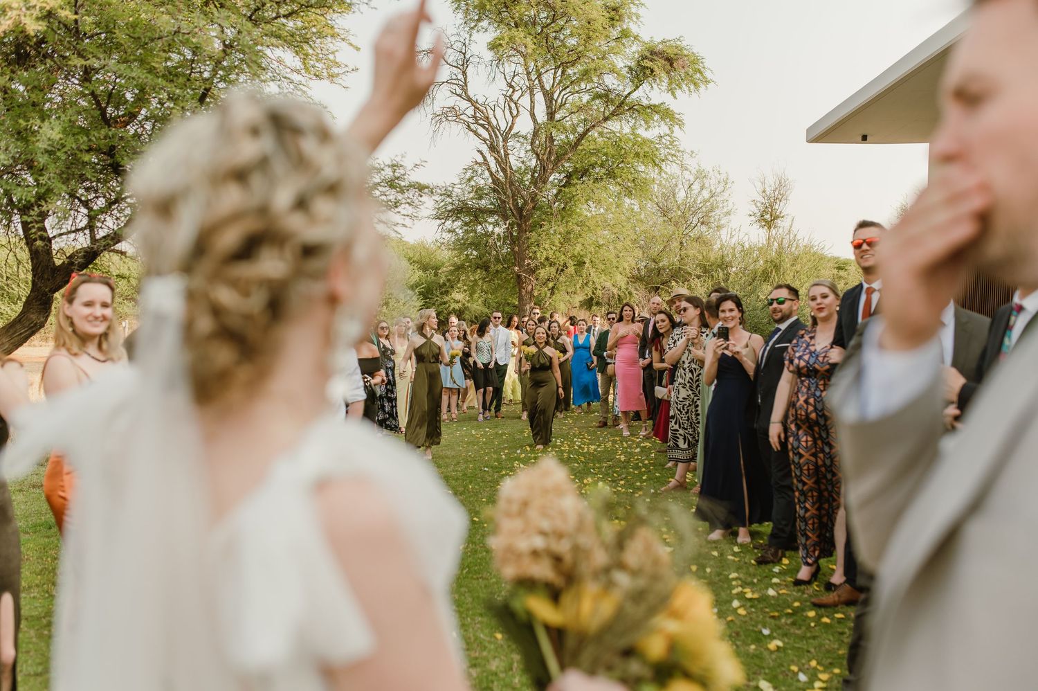 A joyful wedding celebration with guests gathered outdoors during golden hour.
