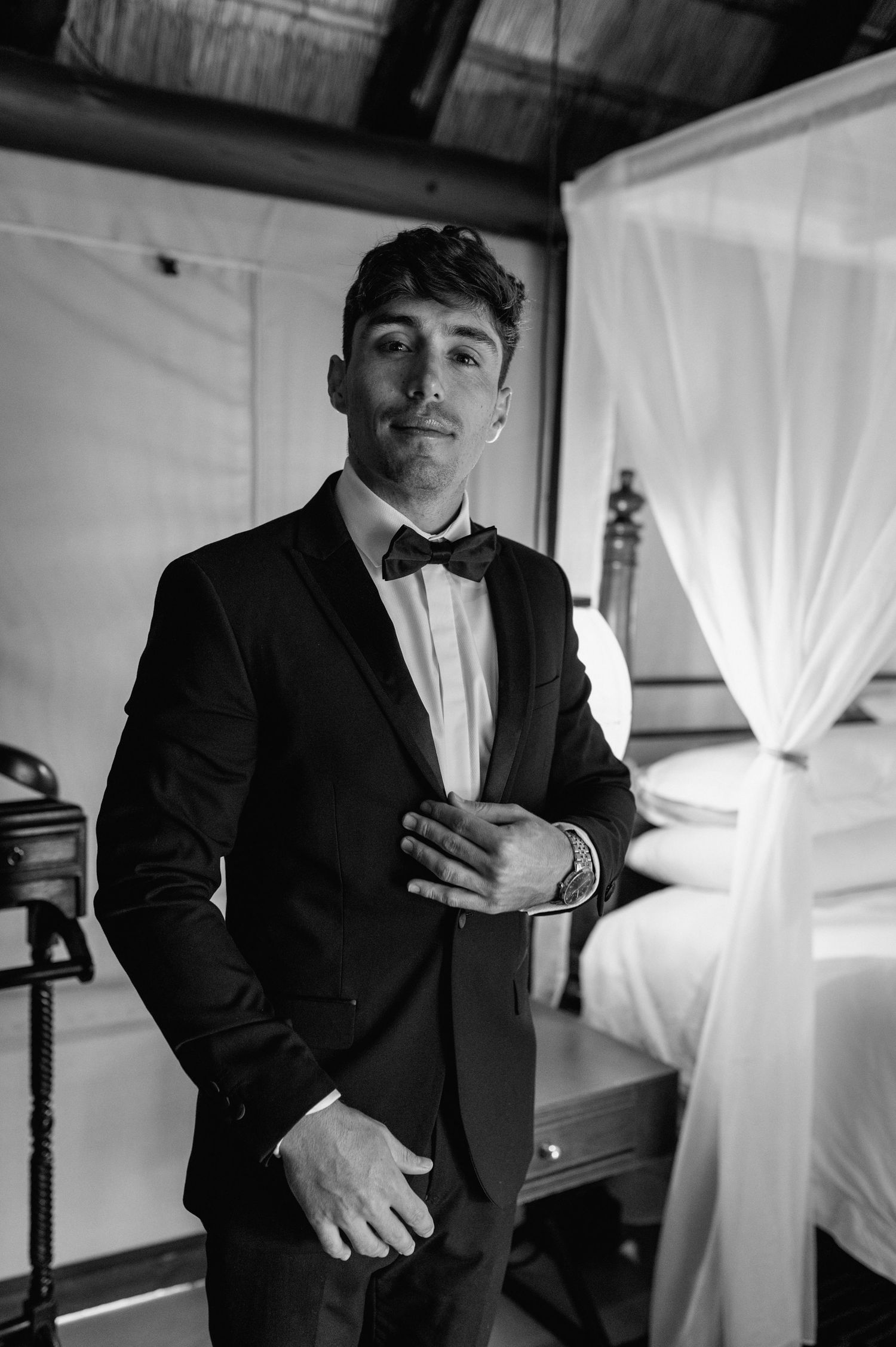 Black and white portrait of someone wearing a classic tuxedo and bow tie in an elegant setting.