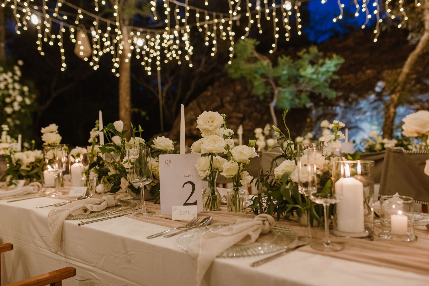 Long banquet tables decorated with white tablecloths and floral centerpieces under twinkling lights.