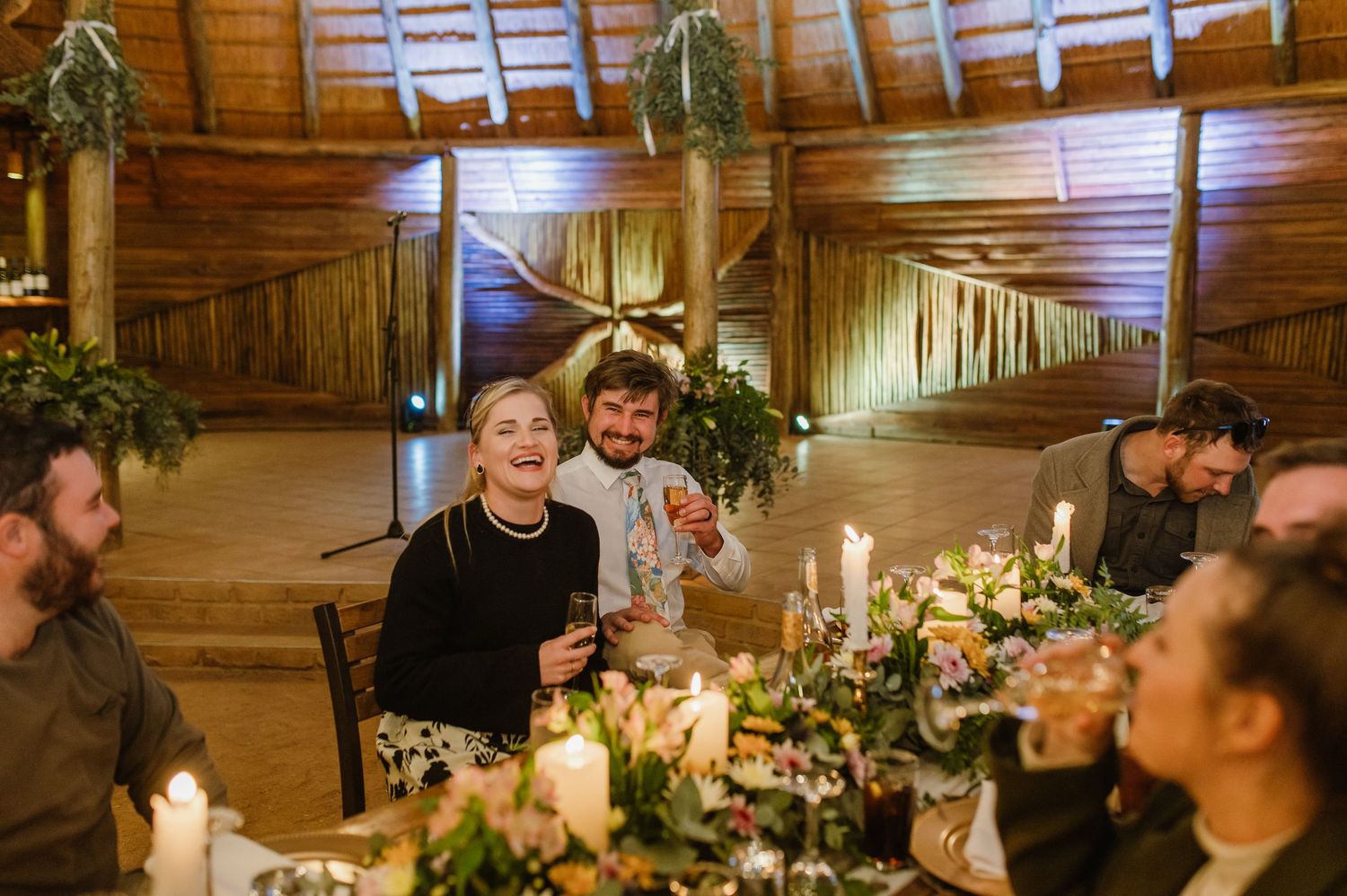Wedding reception tables decorated with floral arrangements and candles in a rustic wooden barn setting.