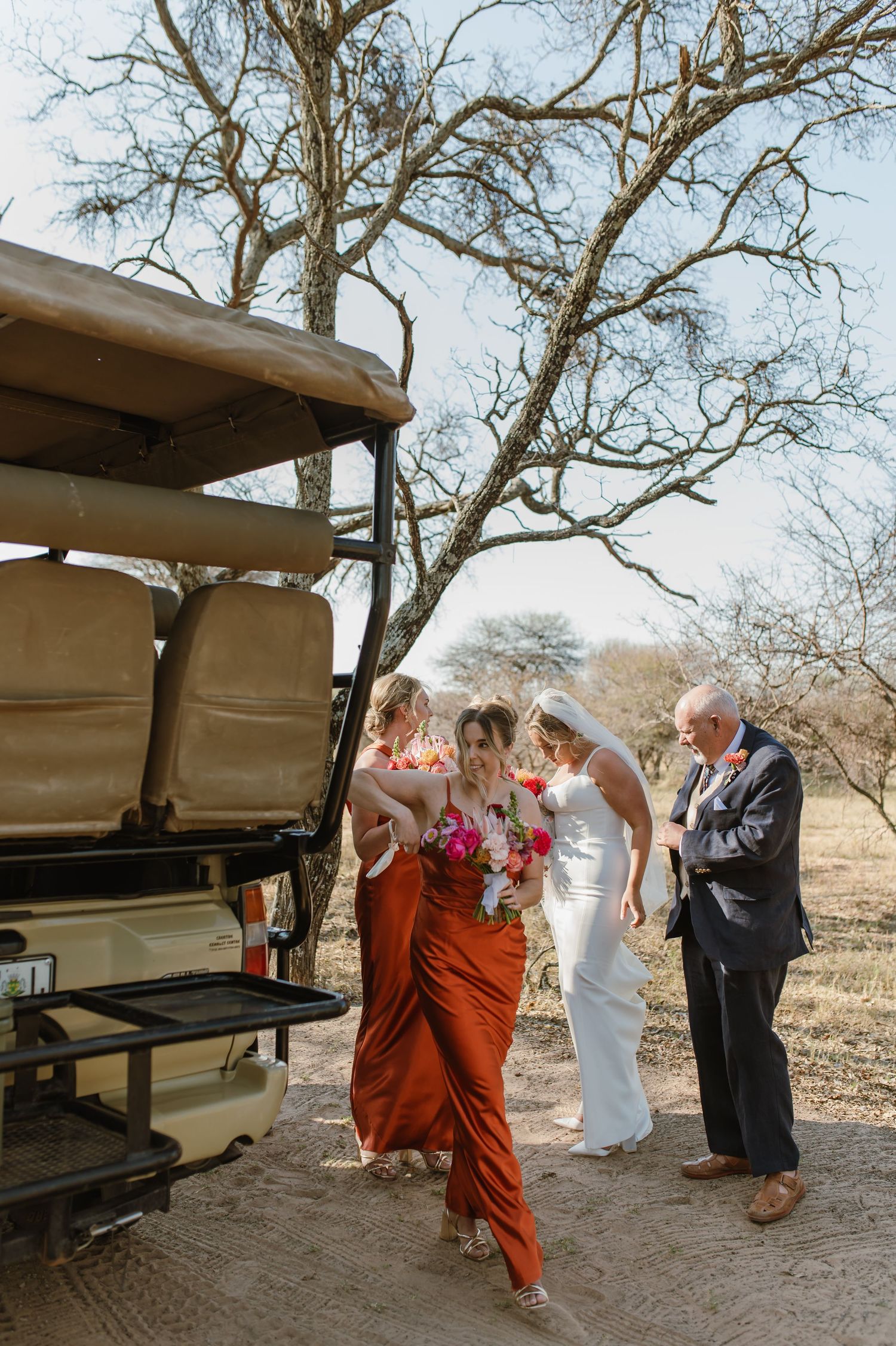 Wedding party helps guests board safari-style vehicles at outdoor venue.