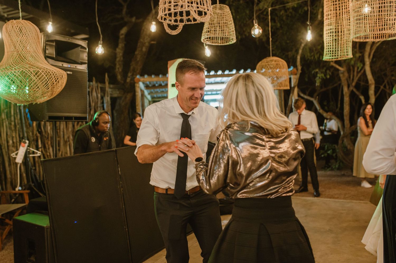 Evening wedding reception features dancing under bohemian-style hanging lanterns and string lights.