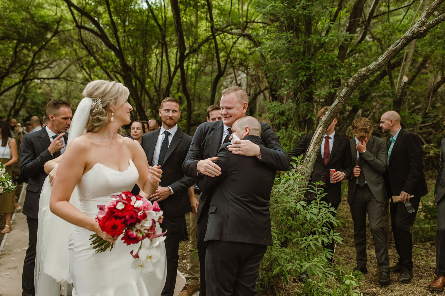 Intimate forest wedding ceremony with guests gathered along a natural pathway.