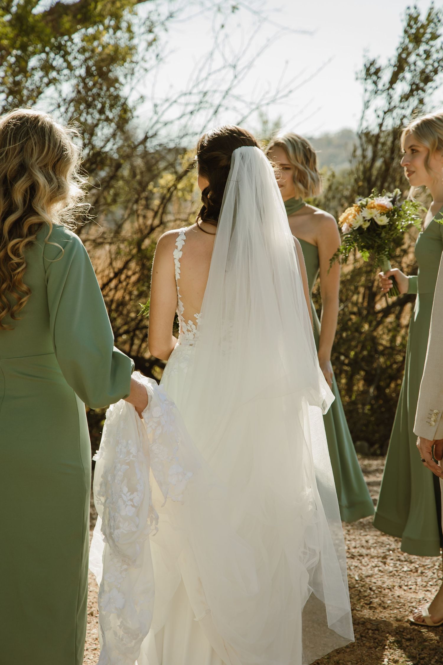 Wedding party in sage green dresses and white gown walking through a desert landscape.
