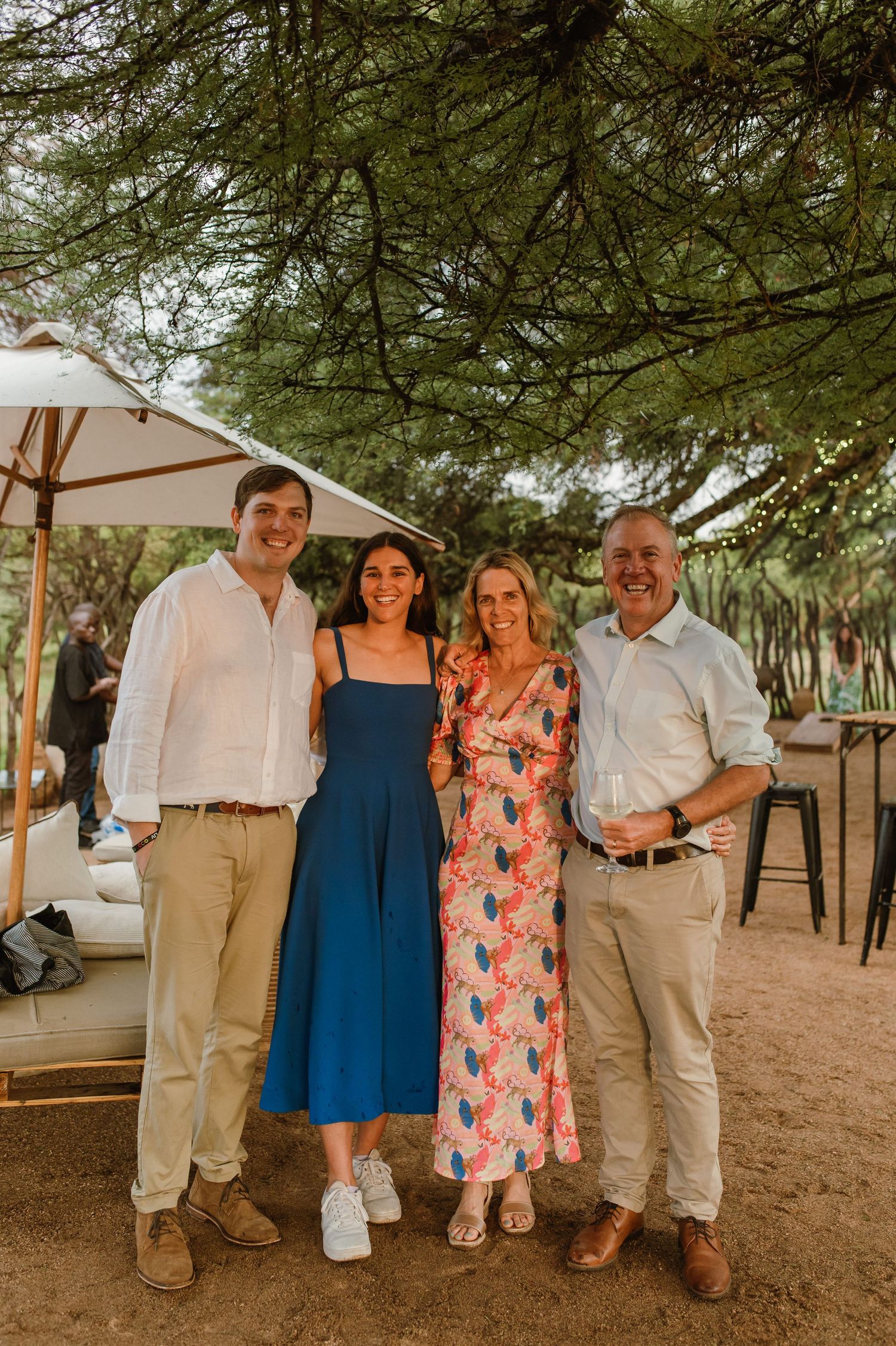 Family members pose together outdoors under trees at a casual summer wedding gathering.