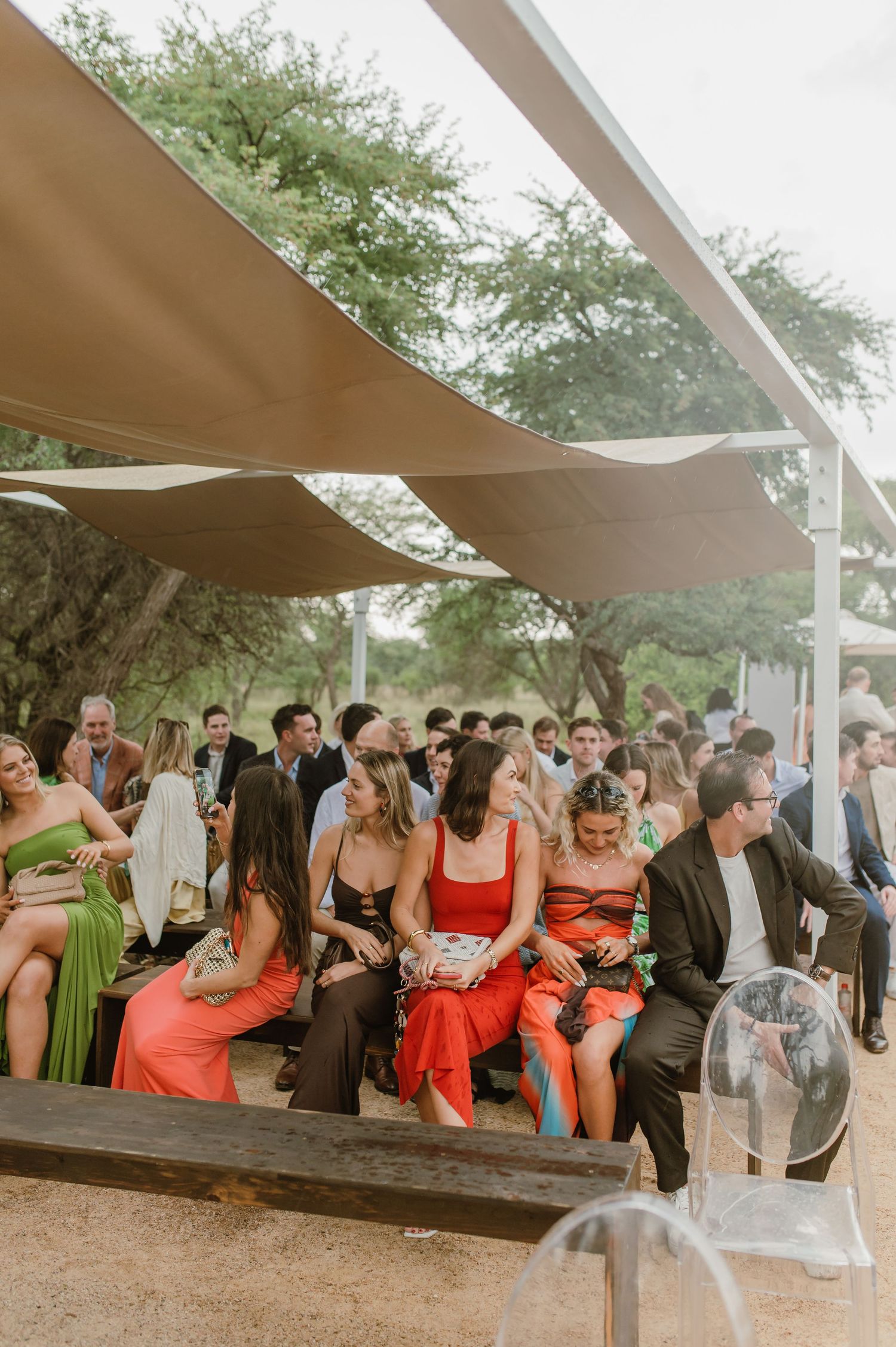 Wedding guests gather under outdoor canopy shade sails during a sunny outdoor celebration.