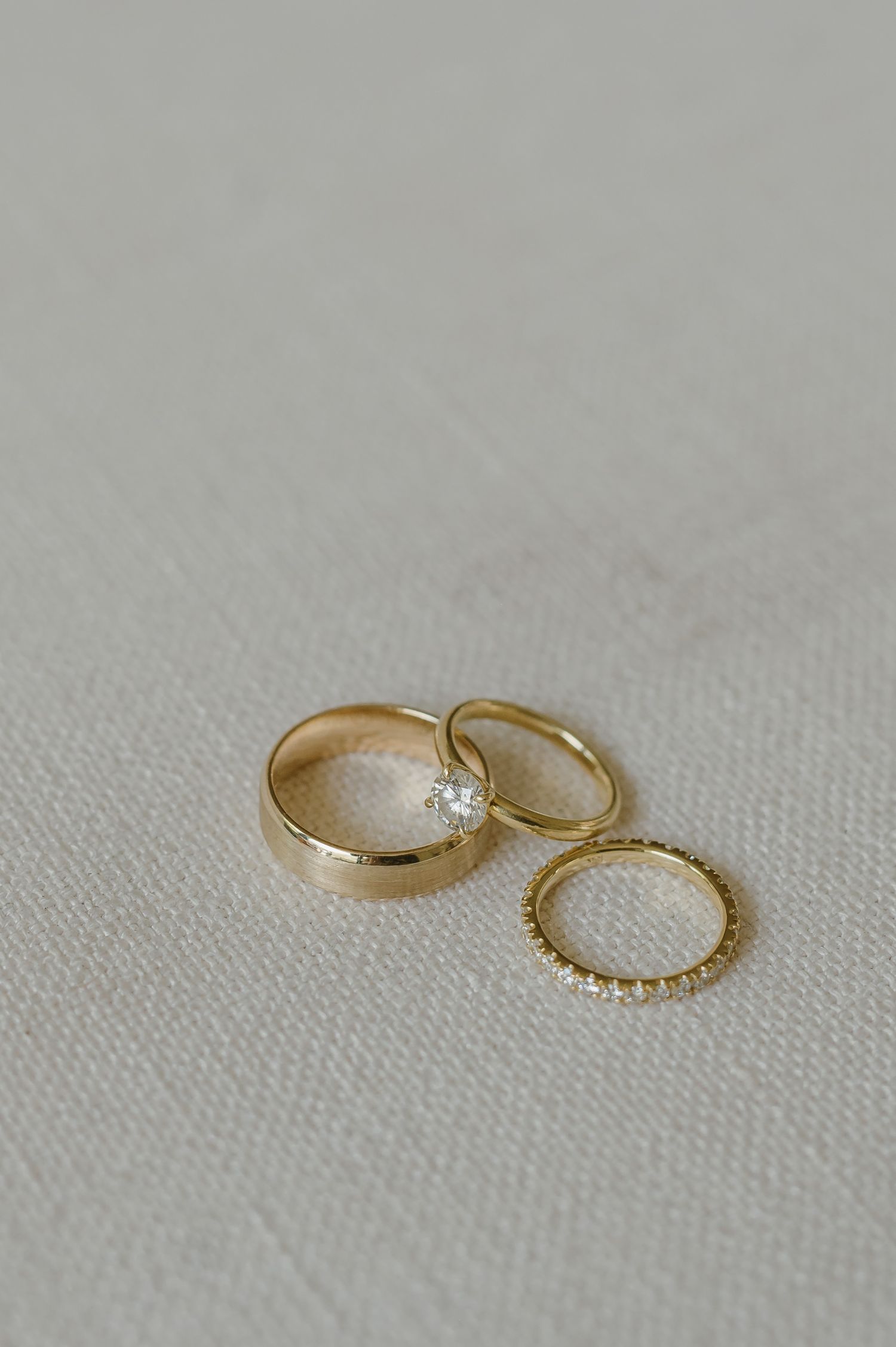 Three gold wedding rings with diamond details arranged on light fabric.