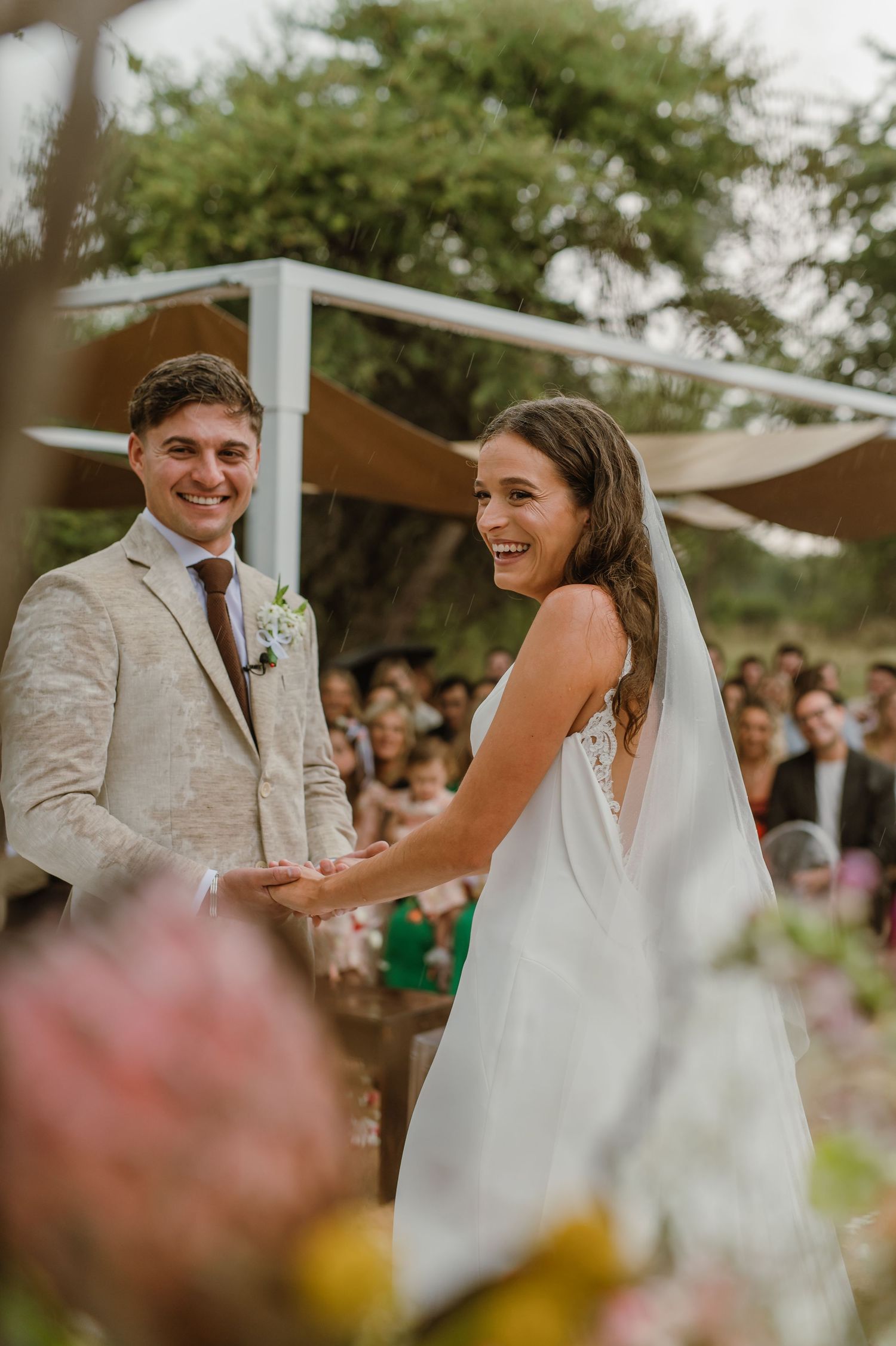 Joyful moments during wedding ceremony under rustic white canopy with desert landscape backdrop.