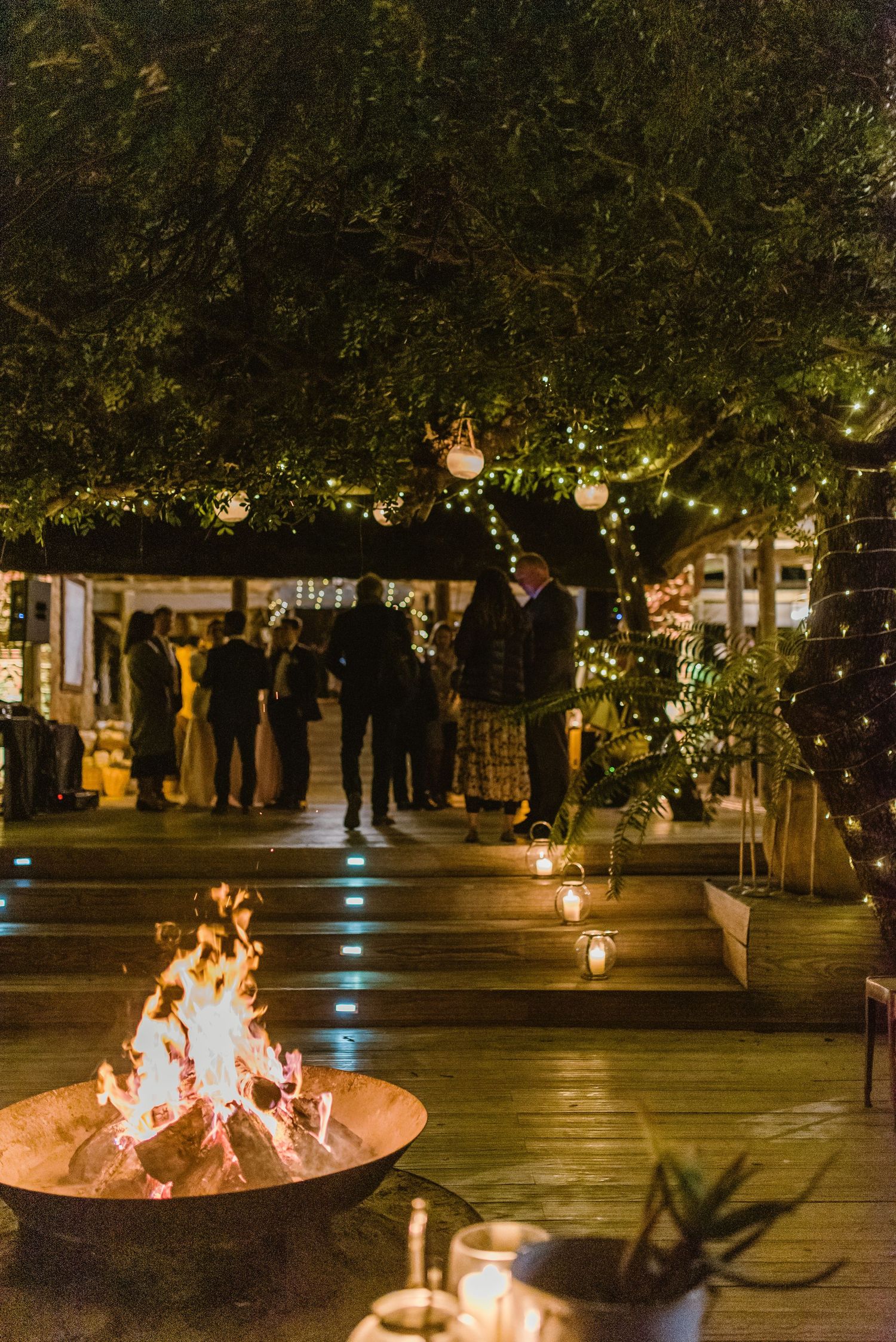 Large fire pit with dancing flames creates ambiance in an outdoor event space.