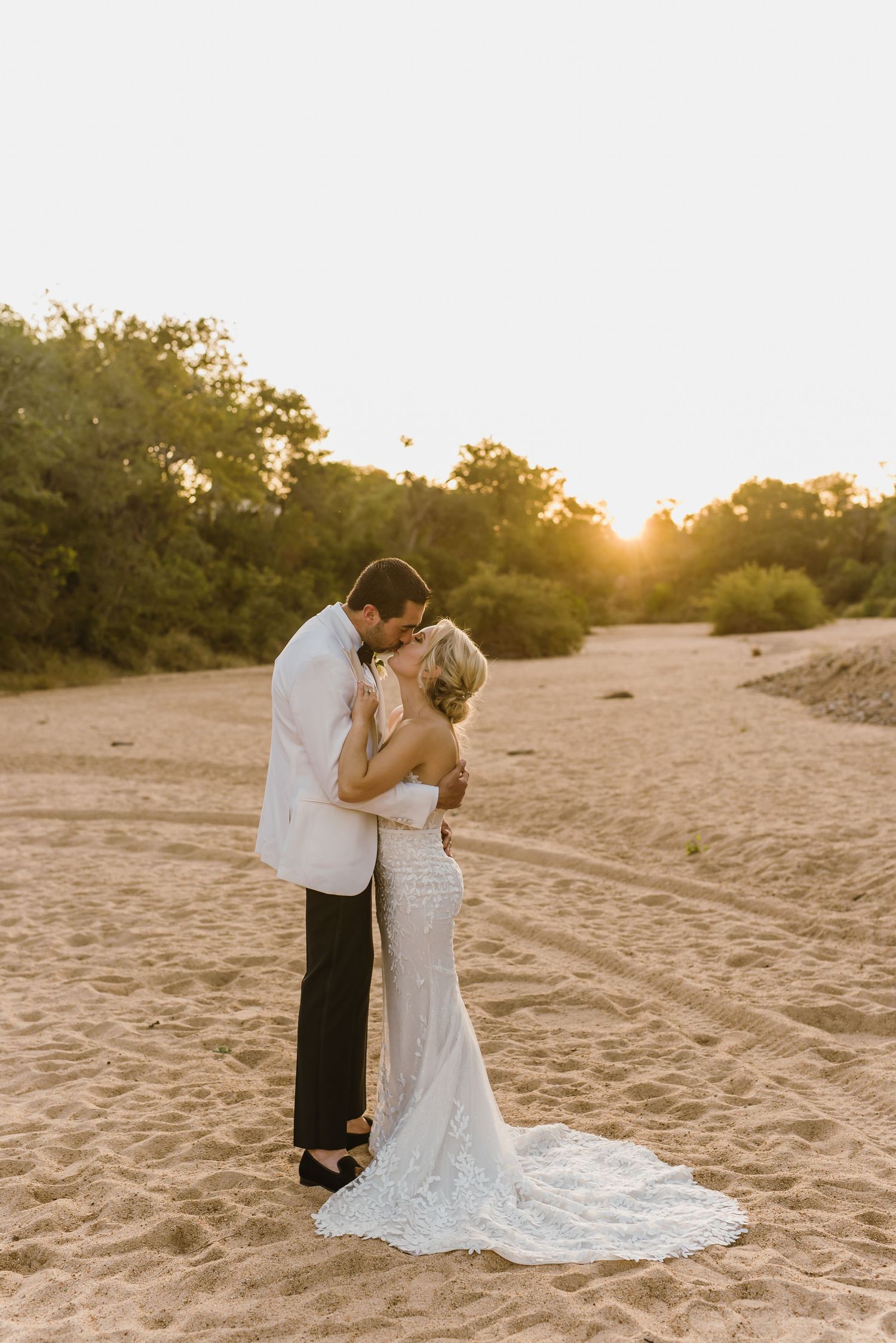 A romantic sunset beach wedding photo shows a couple embracing on sandy dunes at golden hour.
