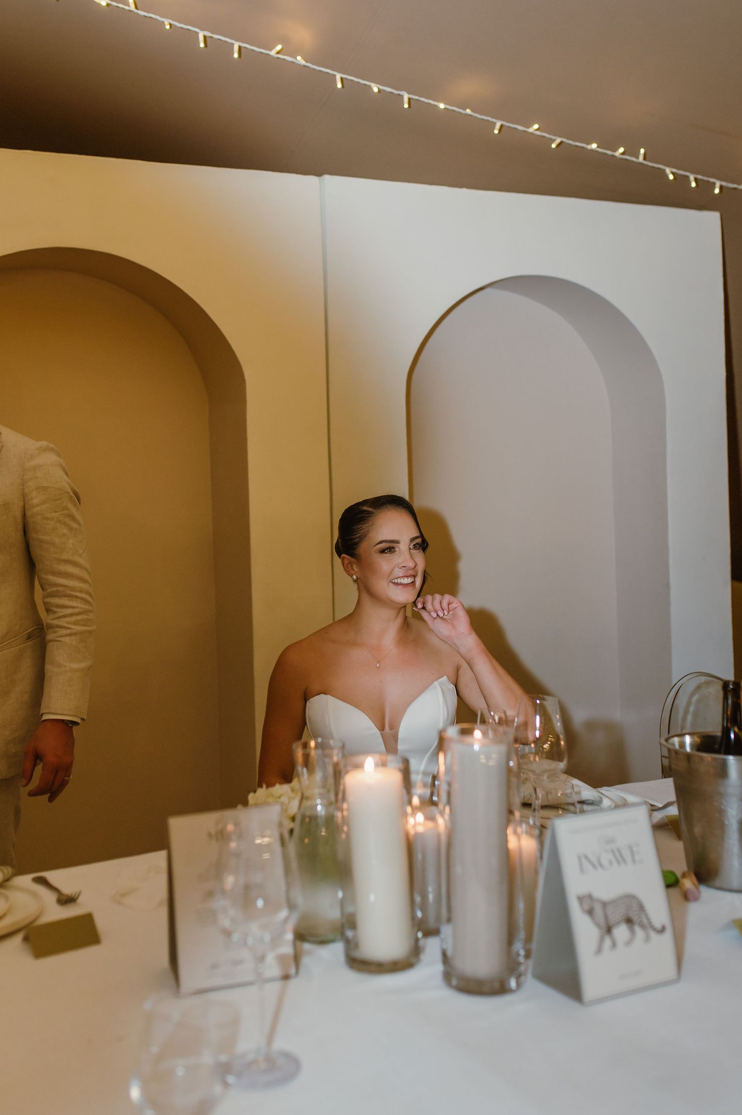 Wedding reception table with white candles and decorative arched backdrop.