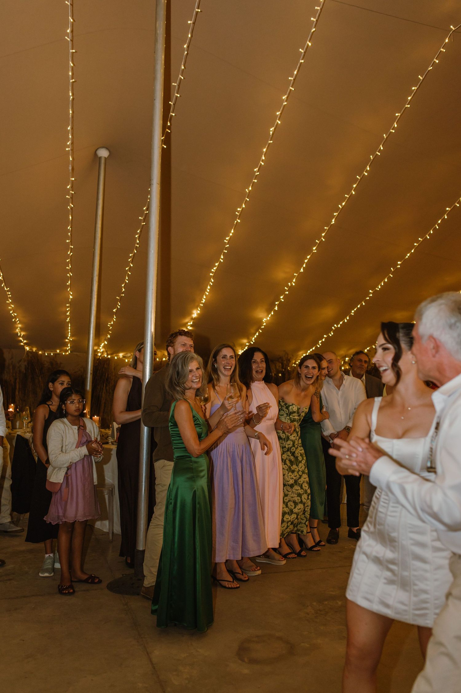 Wedding guests dancing under string lights in a tent during evening reception.