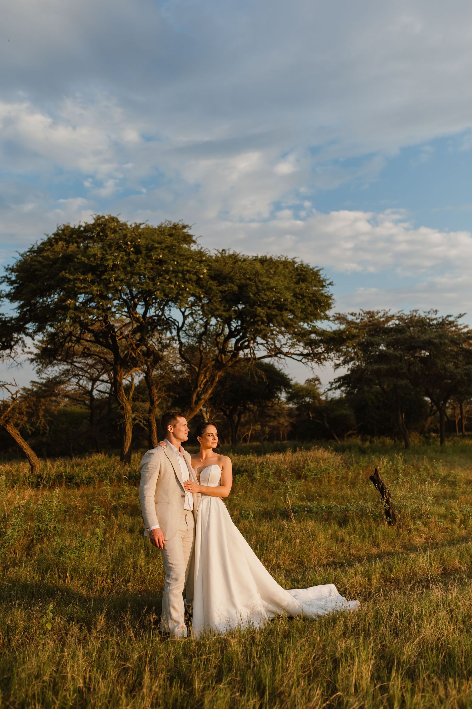 Newlyweds pose together in an open field with majestic acacia trees in the background.