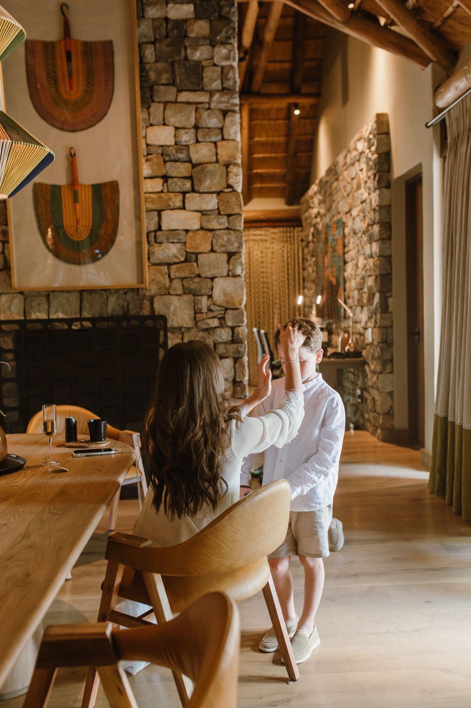 Woman styling a boys hair in a rustic stone fireplace lodge dining room.