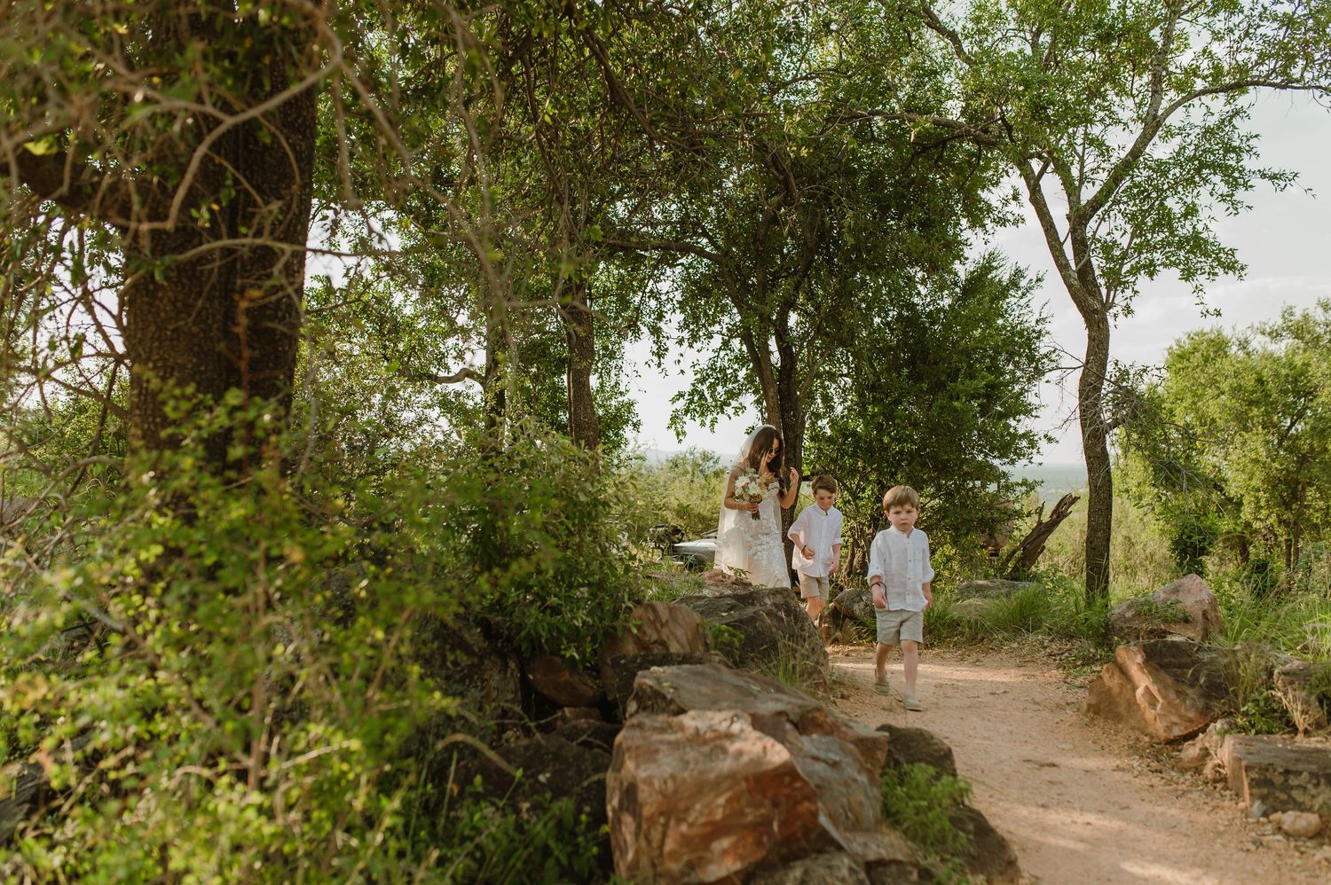 Wedding guests walking along a scenic rocky path surrounded by lush green trees and bushveld.
