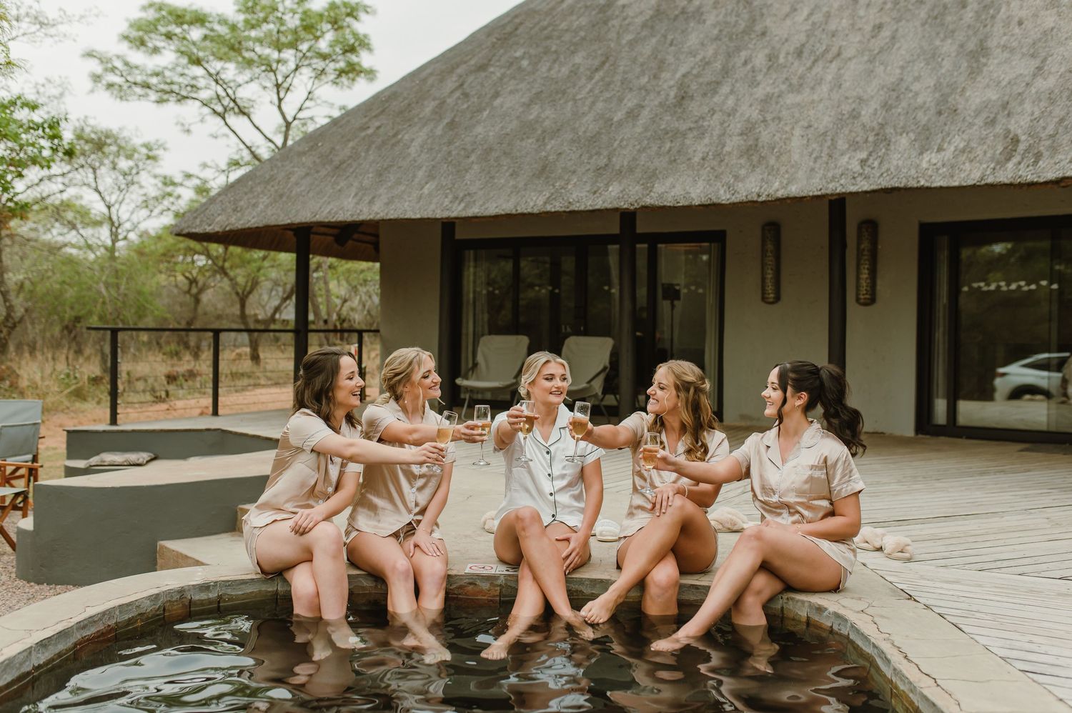 Group in coordinated loungewear sits casually on edge of wooden deck at safari lodge.