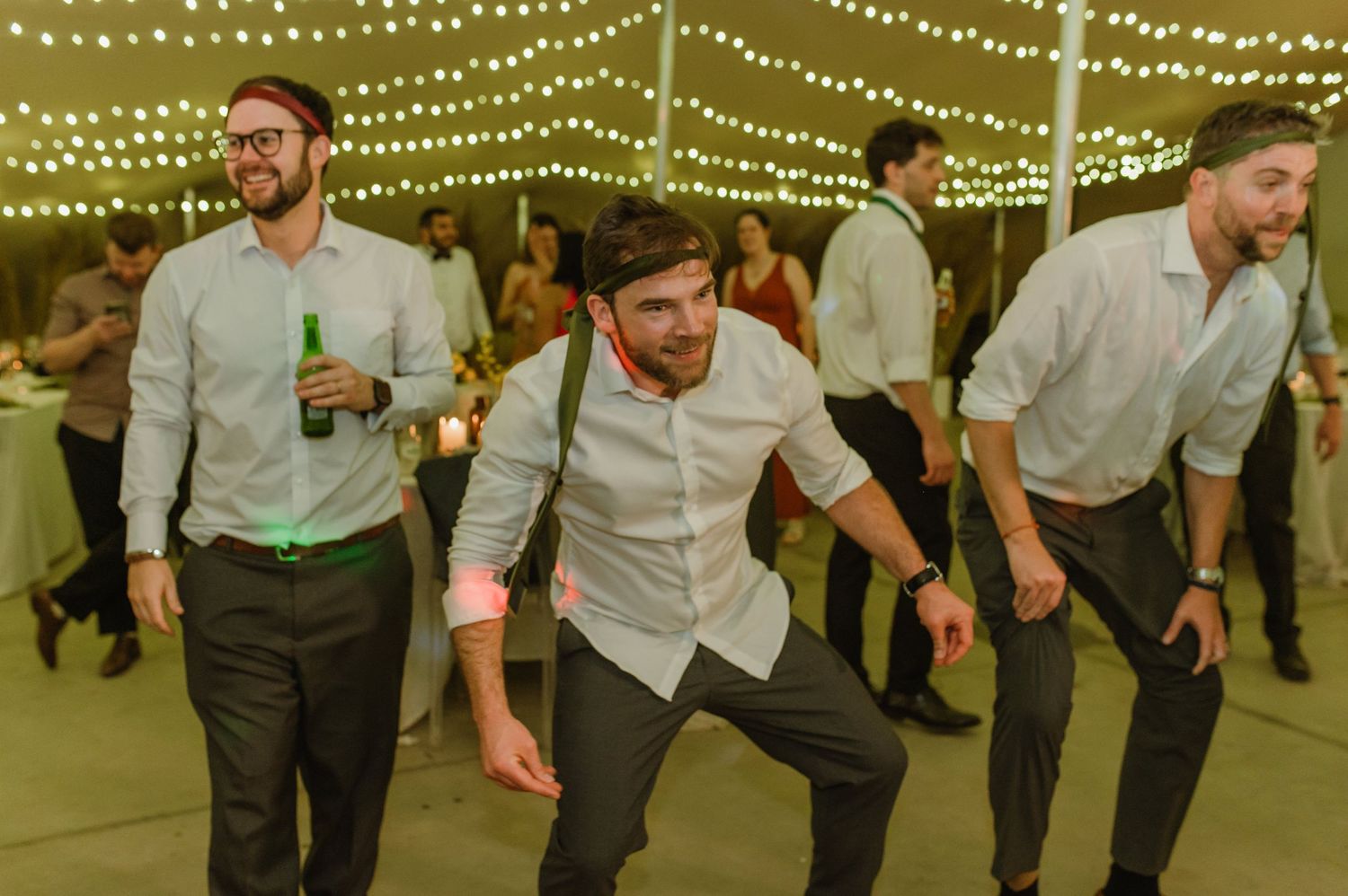 Wedding guests performing synchronized dance moves under string lights.