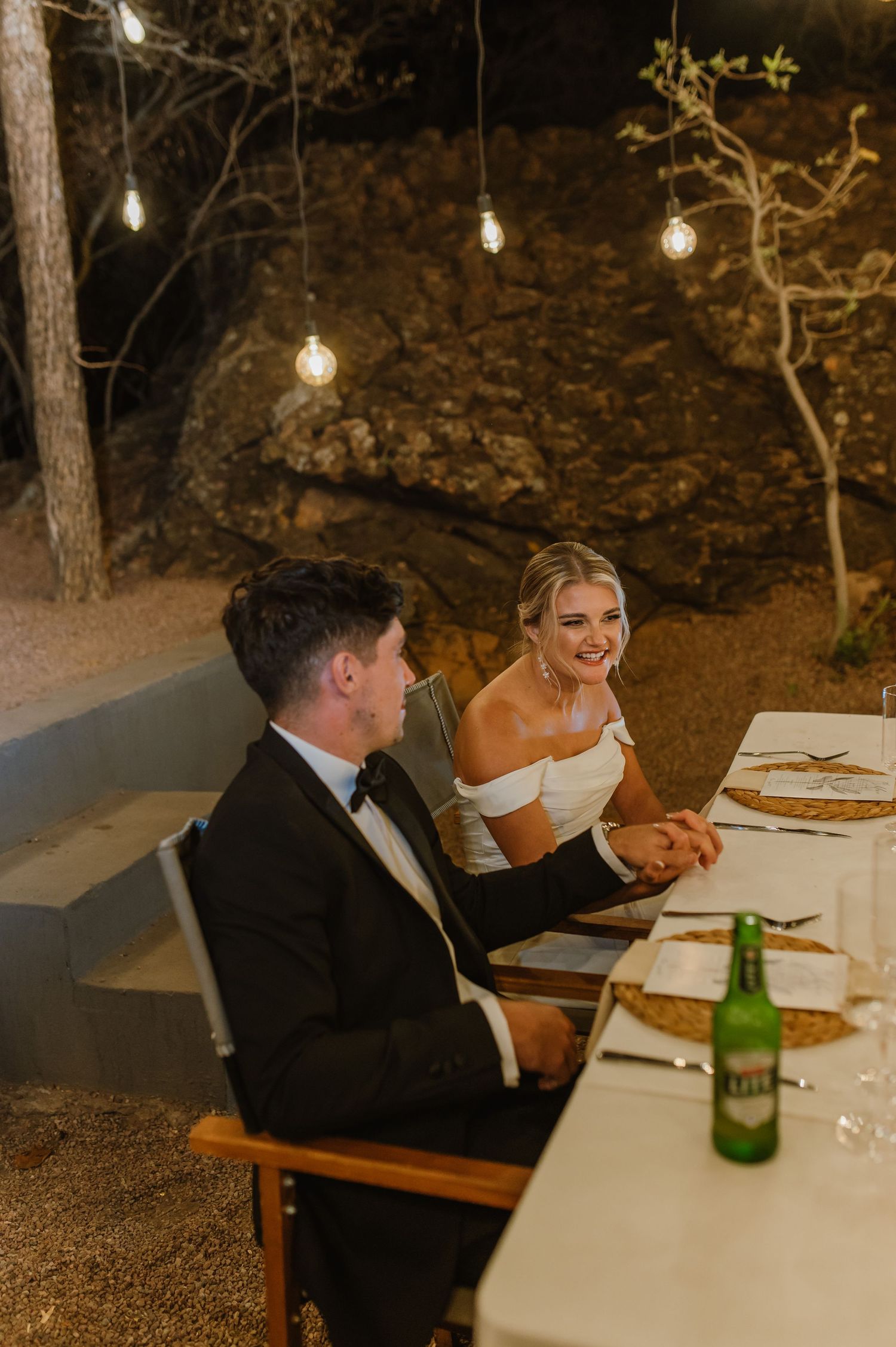 Couple enjoying an intimate dinner under string lights at an outdoor wedding reception.