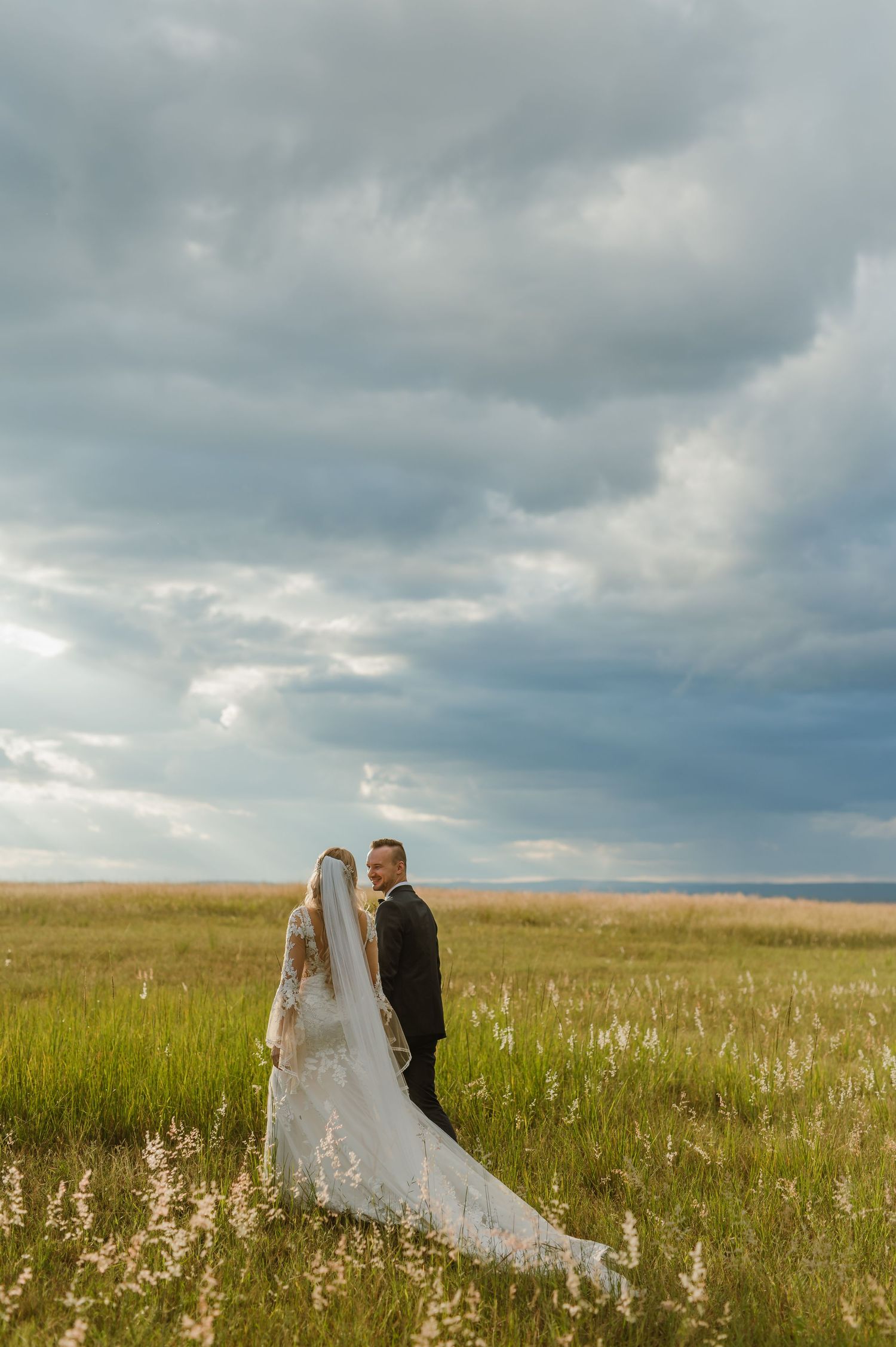 Wedding couple standing in a vast prairie field under dramatic cloudy skies.