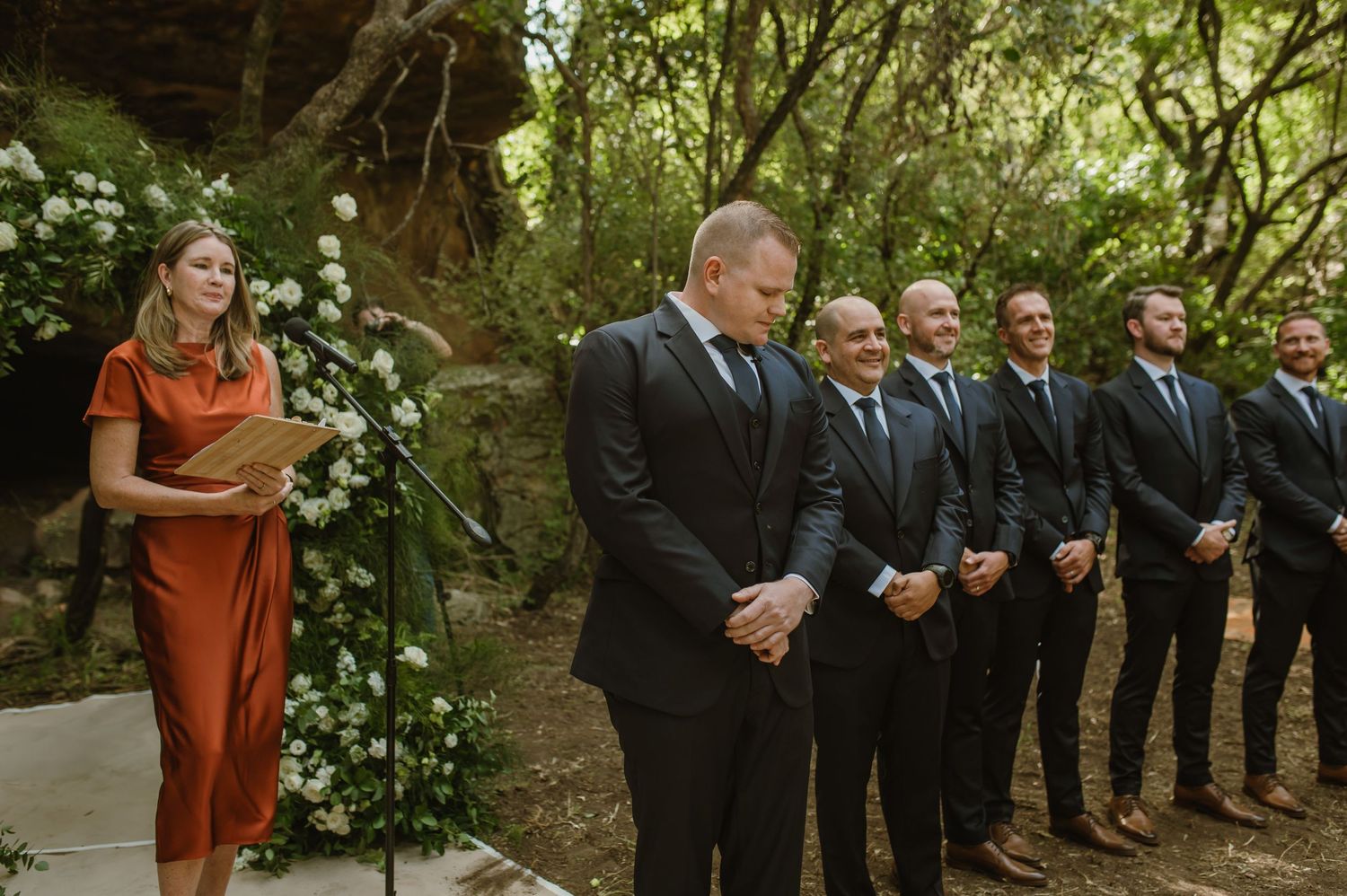 Wedding ceremony processional in a natural forest setting with formal attire.
