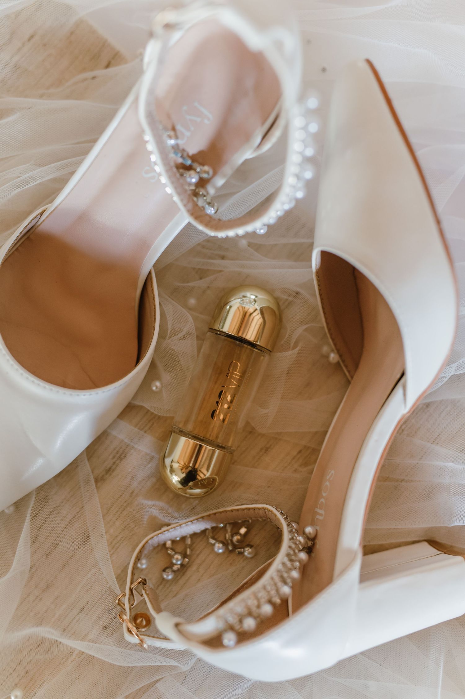 Elegant bridal accessories including pearl jewelry and white shoes on light wooden floor.