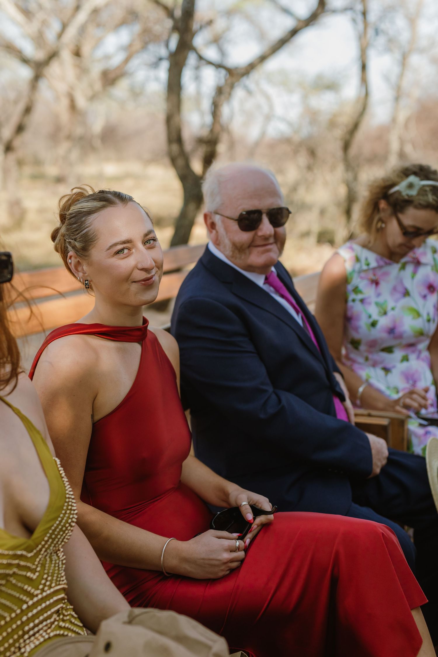 Wedding attendees in red and formal attire enjoy a relaxed moment on outdoor seating.
