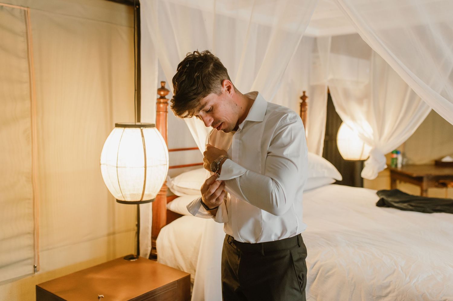 Getting dressed in formal attire near a white canopy bed with ambient lighting.