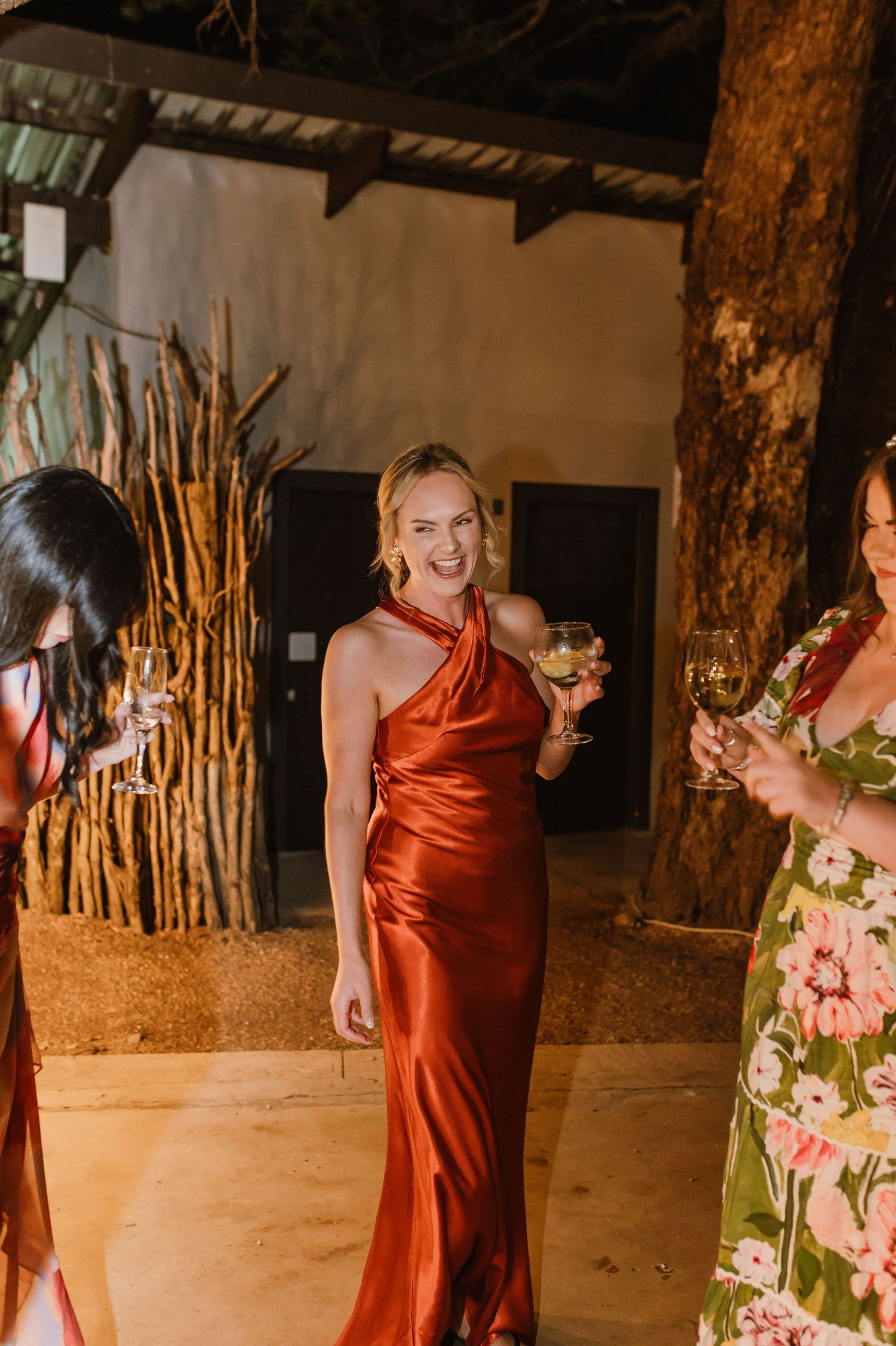 Wedding attendees in red dresses enjoying drinks and conversation at an outdoor reception.