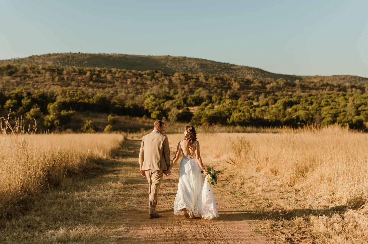 Wedding party walking through scenic field with mountains and sunset backdrop.