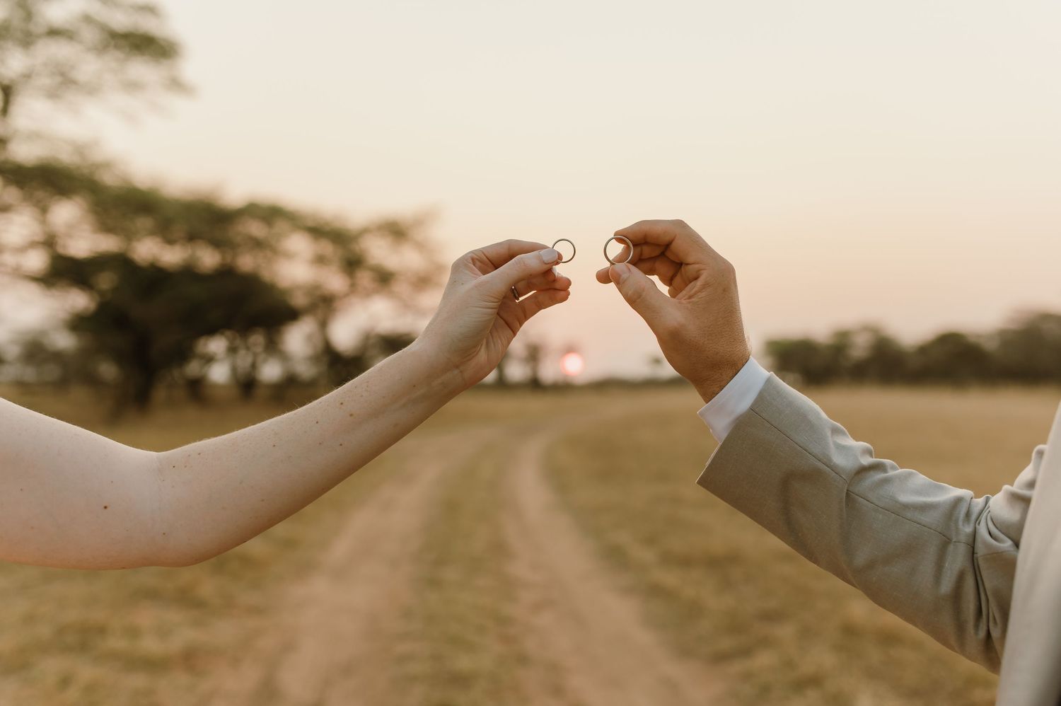 Newlyweds hold hands while walking down a dirt path at sunset in a romantic outdoor setting.