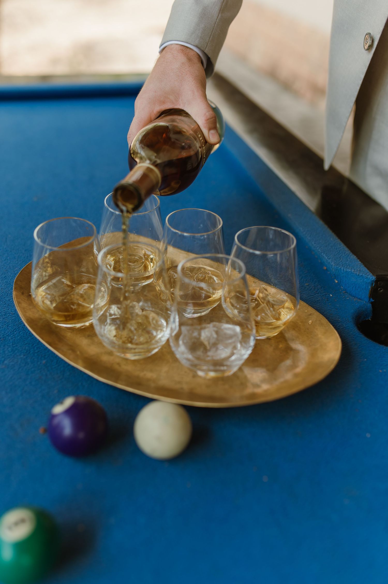 Close-up of drinks being poured onto a golden tray with glasses and pool balls.