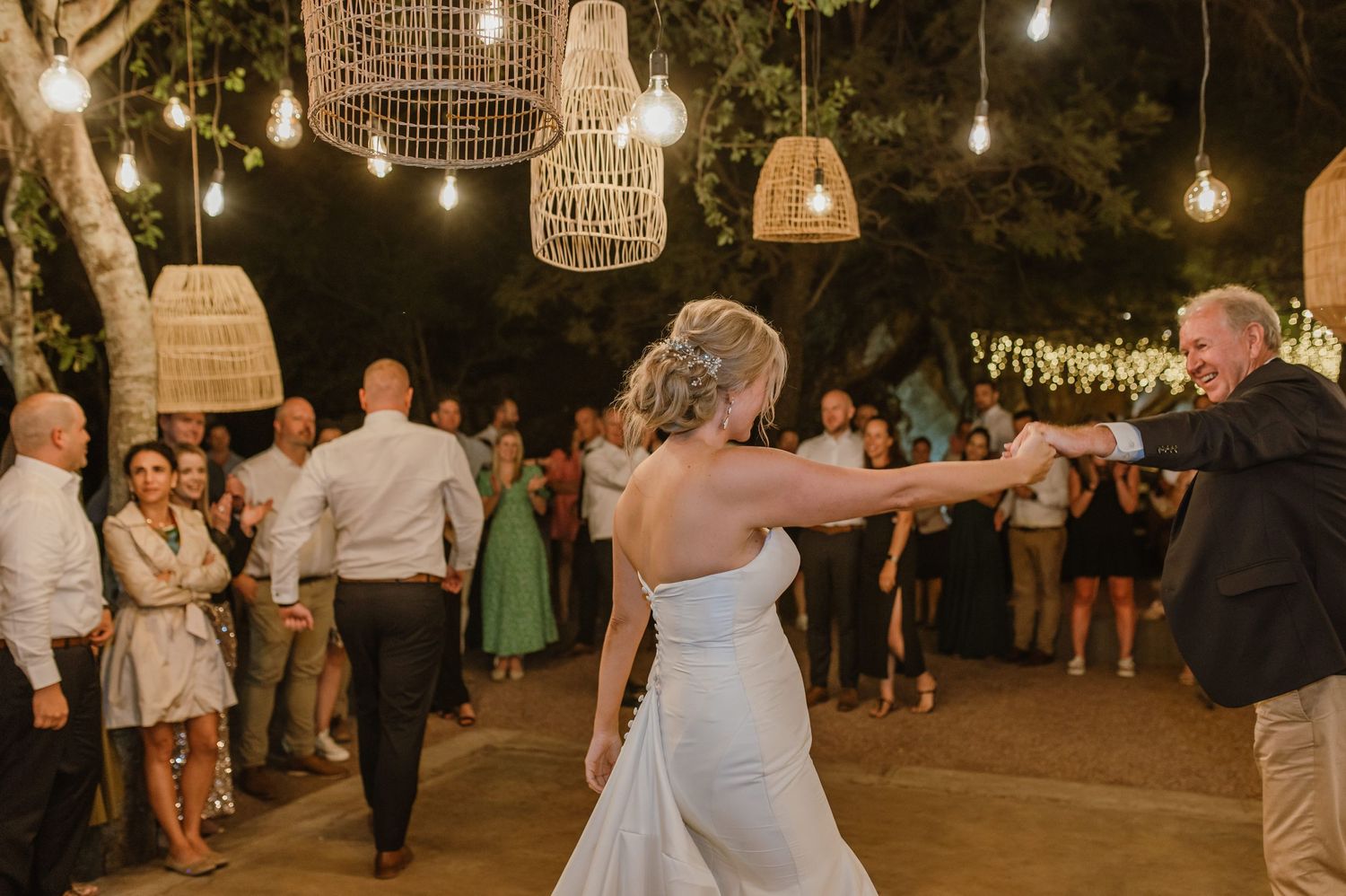 Couple dancing under hanging rattan lanterns and string lights at an outdoor wedding reception.