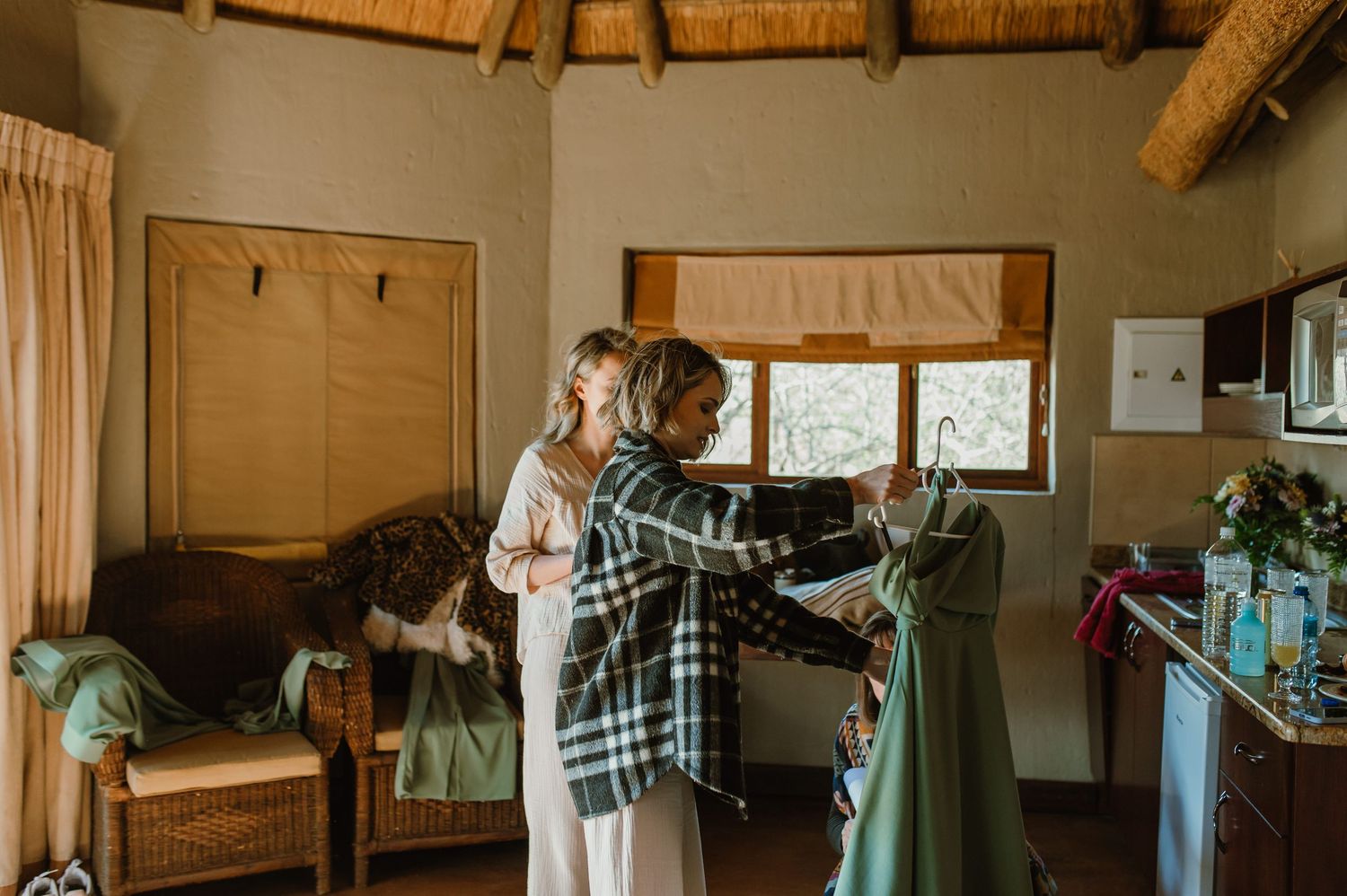 Interior view of thatched roof lodge with hanging clothes and natural light.