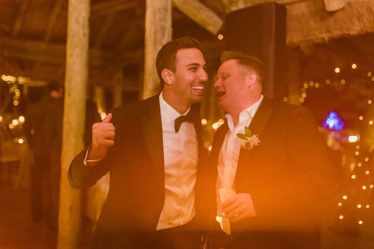 Party guests dancing and celebrating at an evening reception in a warmly lit barn.