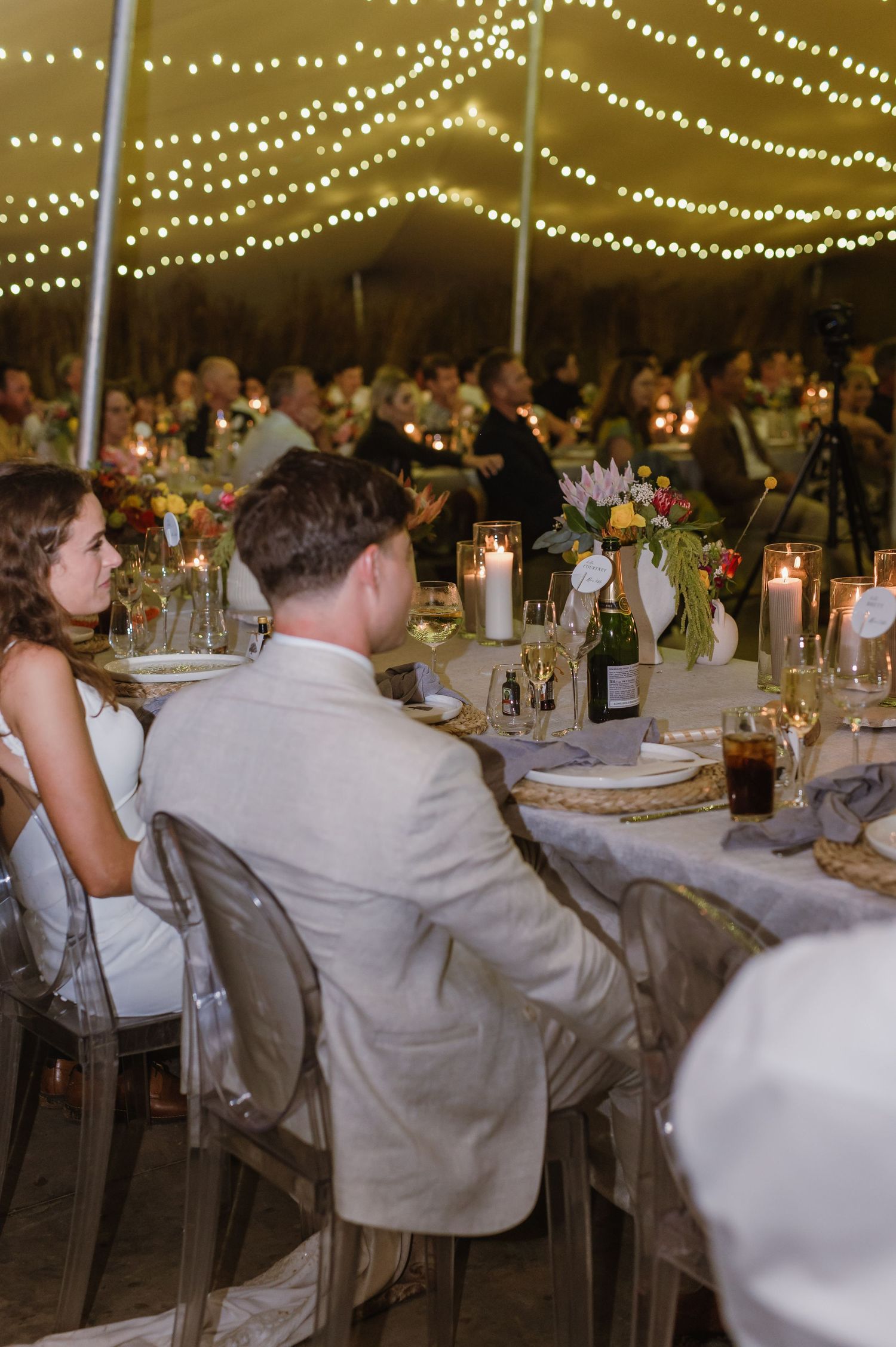 Long banquet tables set with candles and floral centerpieces under twinkling lights at an evening wedding reception.
