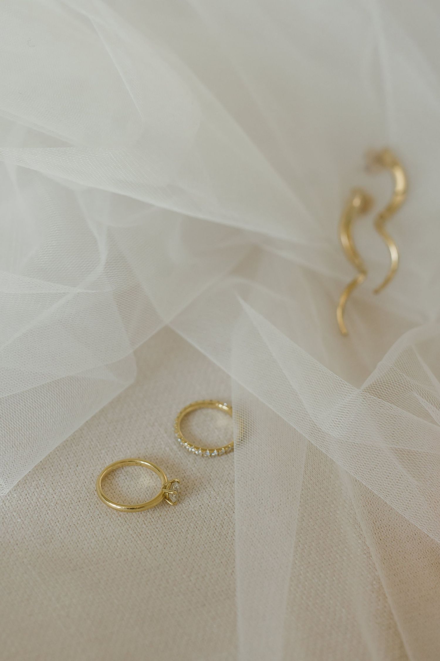 Elegant gold wedding rings and jewelry displayed on white tulle fabric.