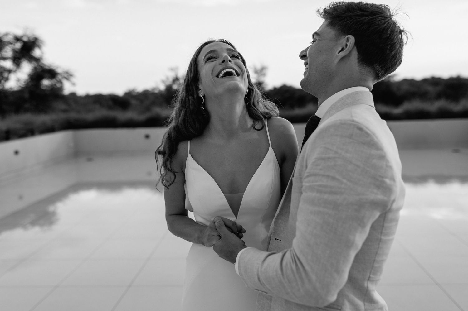 A black and white portrait of a couple laughing together in wedding attire.