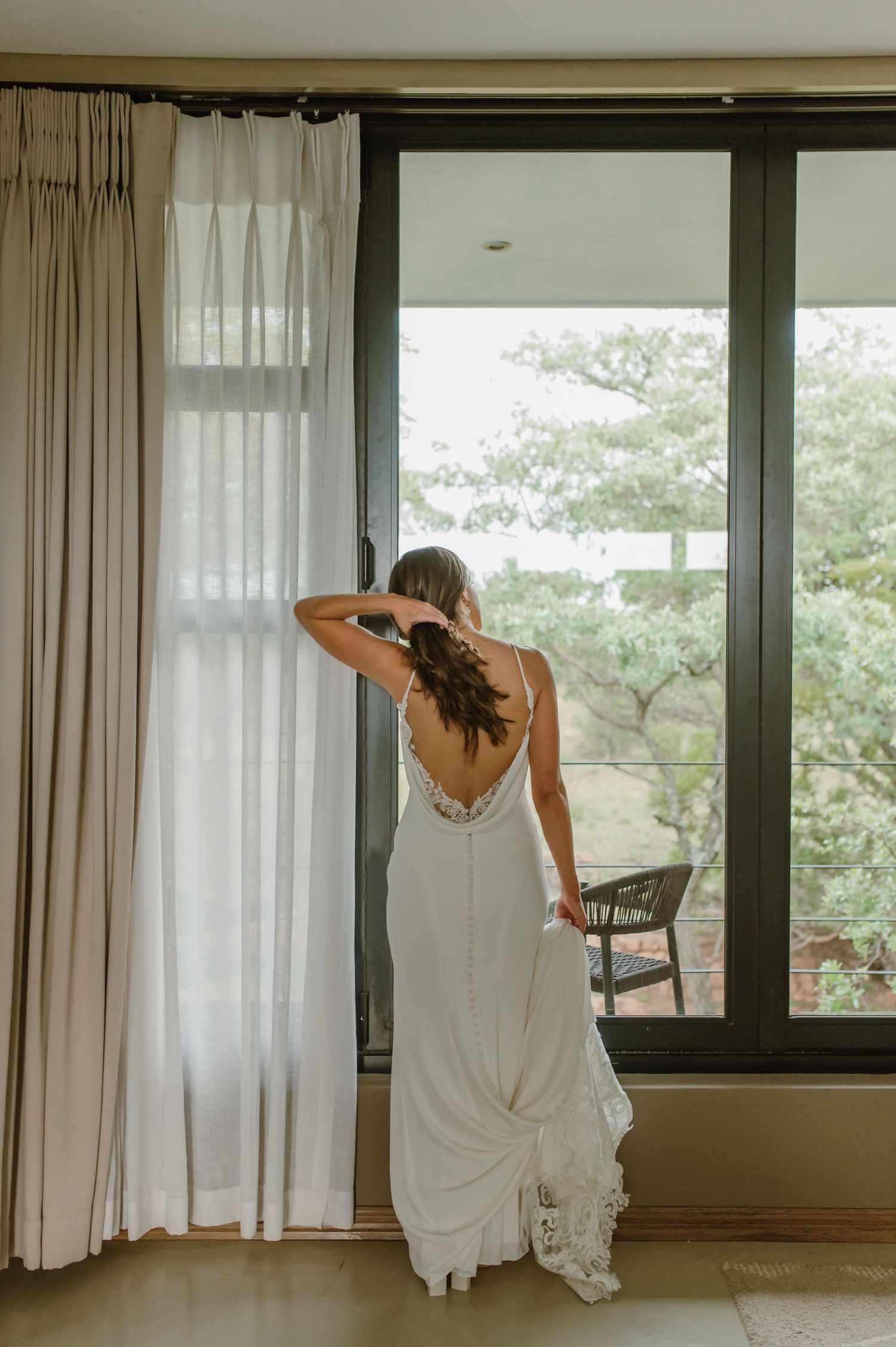 A white-clad figure dances gracefully in front of large windows with sheer curtains in a modern interior space.